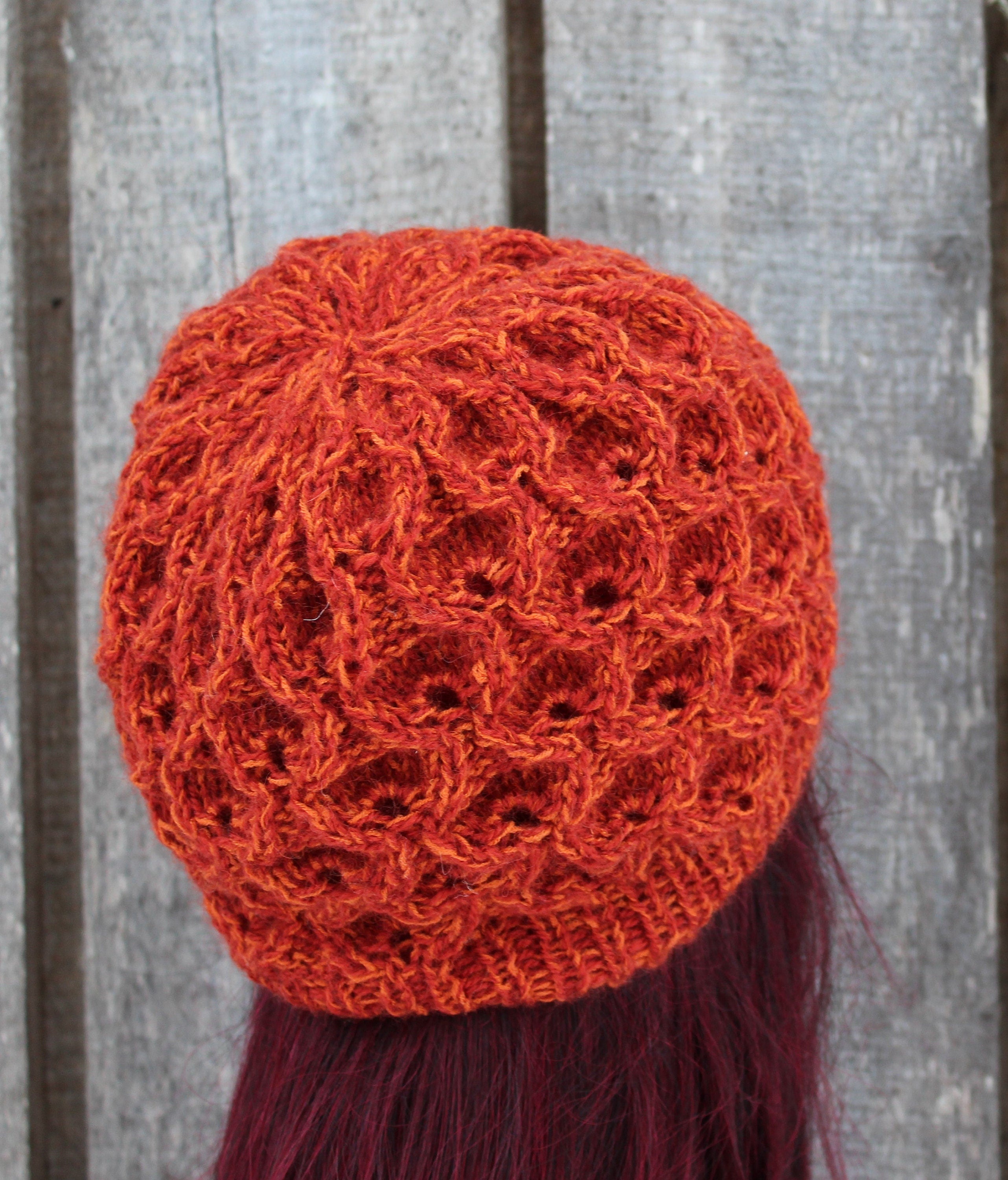 Orange knitted hat on a person with red hair against a wooden background
