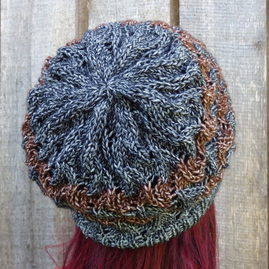 Knitted hat with braided pattern and red tassel on a wooden background