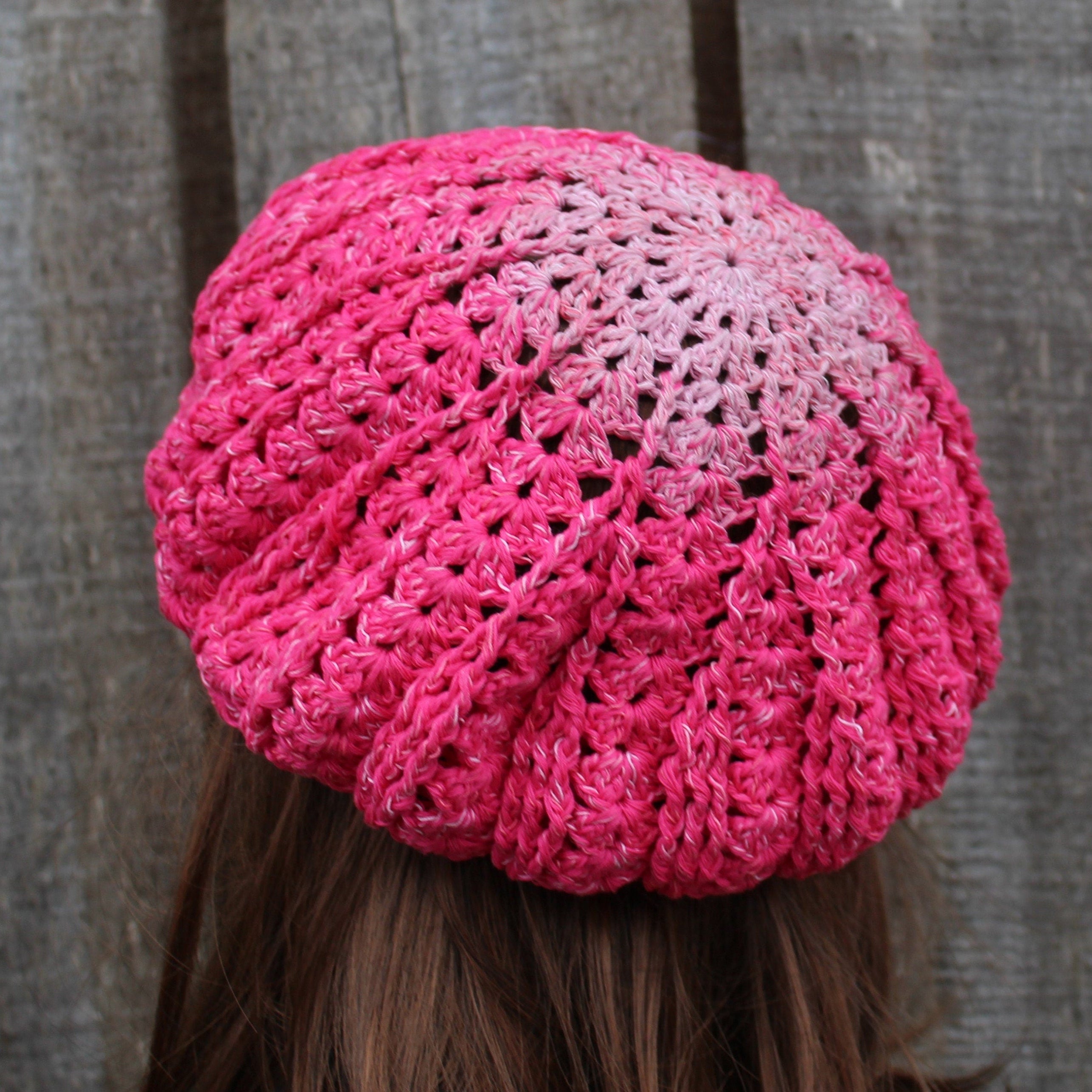 Pink crocheted beanie worn by a person against a wooden background