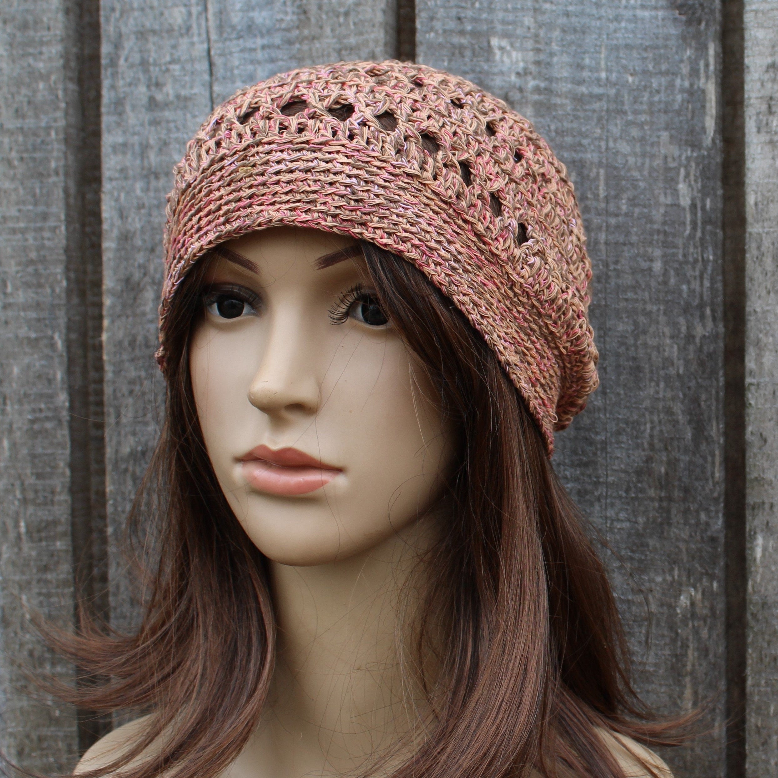 Mannequin head wearing a pink crochet hat against a wooden background