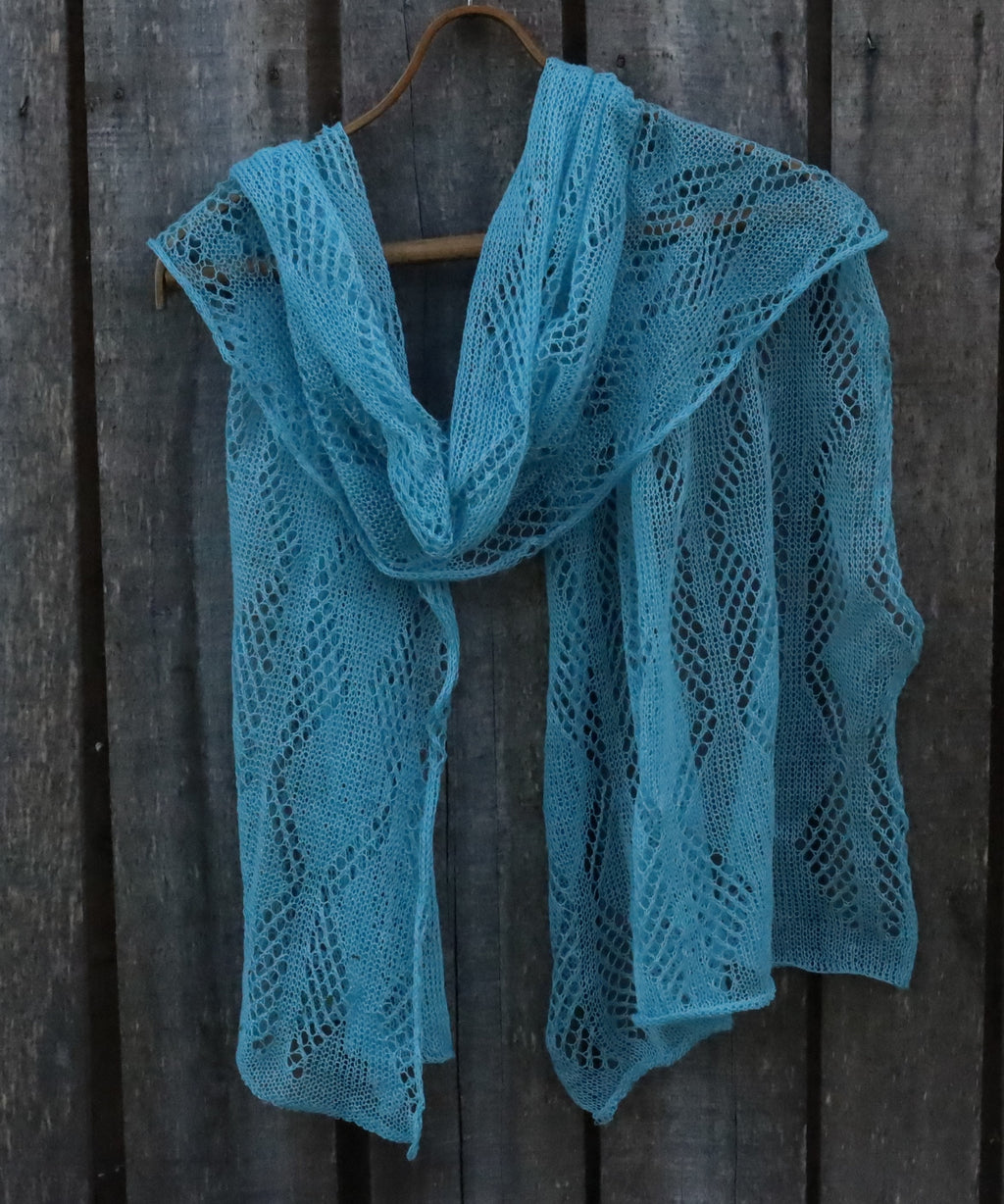 Blue knitted shawl on a wooden hanger against a wooden background