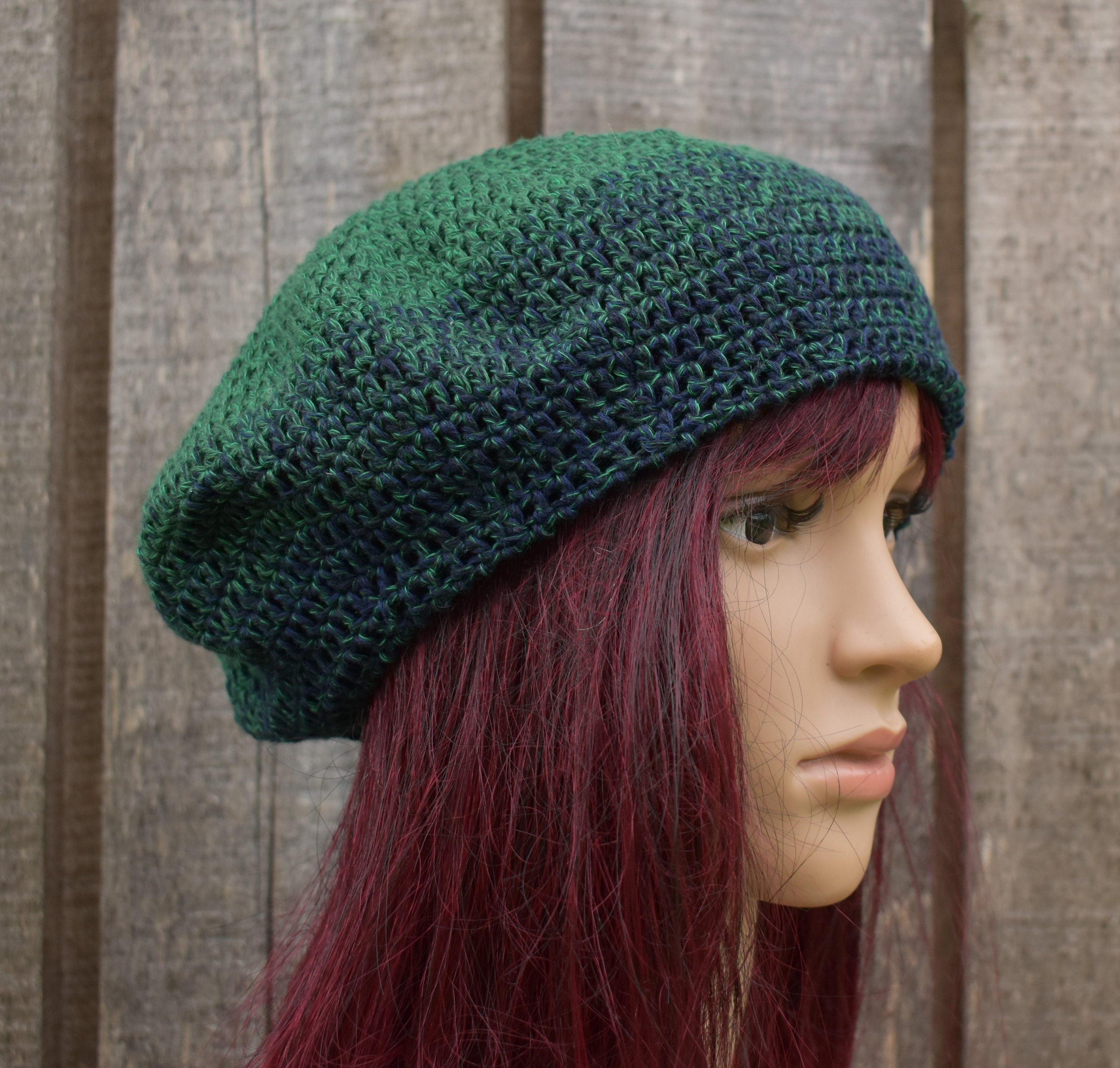 Green knitted beret on a mannequin head with red hair against a wooden background