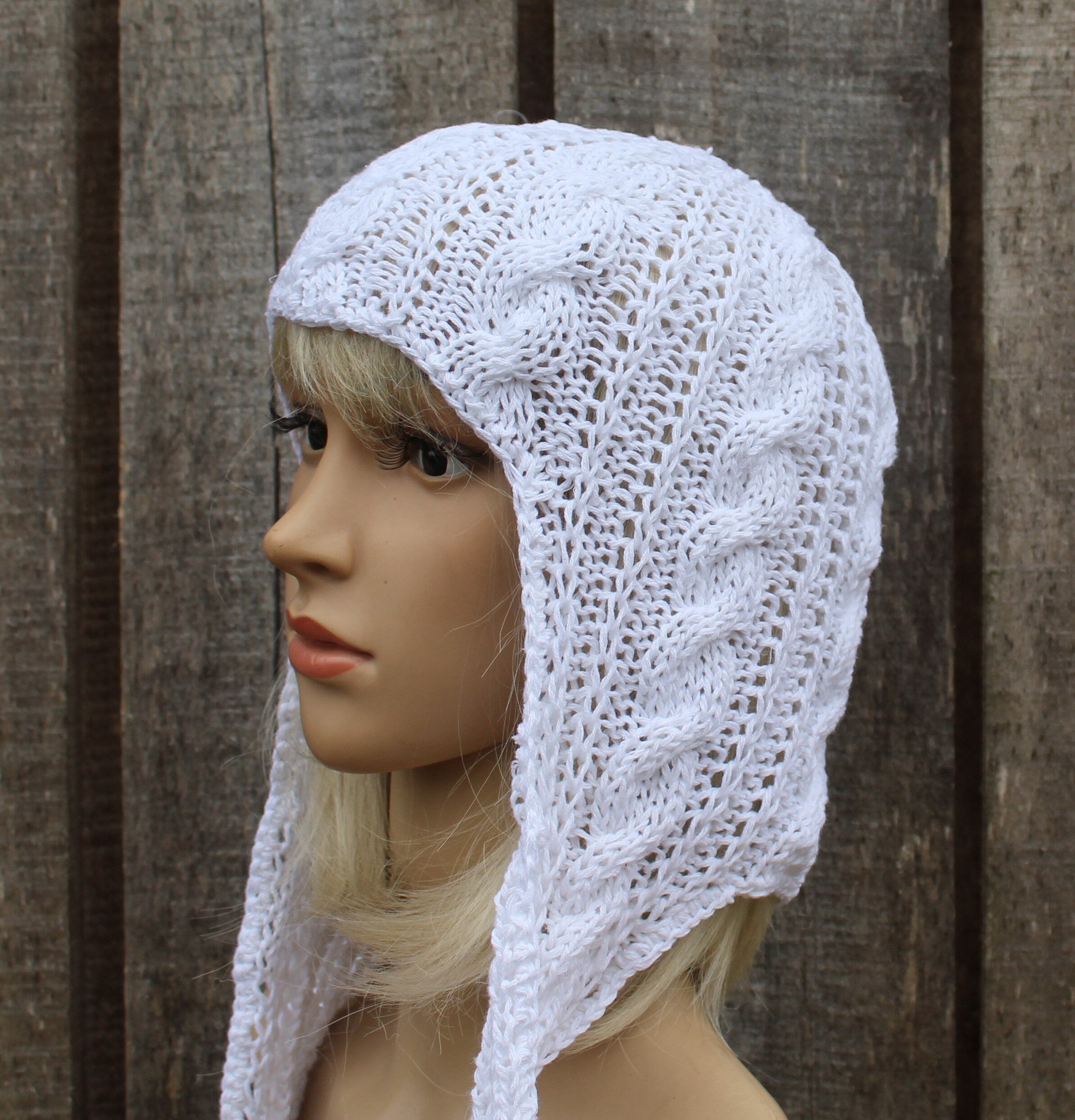 Mannequin head wearing a white knitted hood against a wooden background