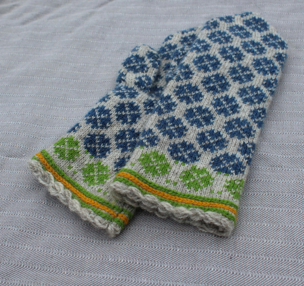 Knitted mittens with blue and green pattern on a gray fabric background