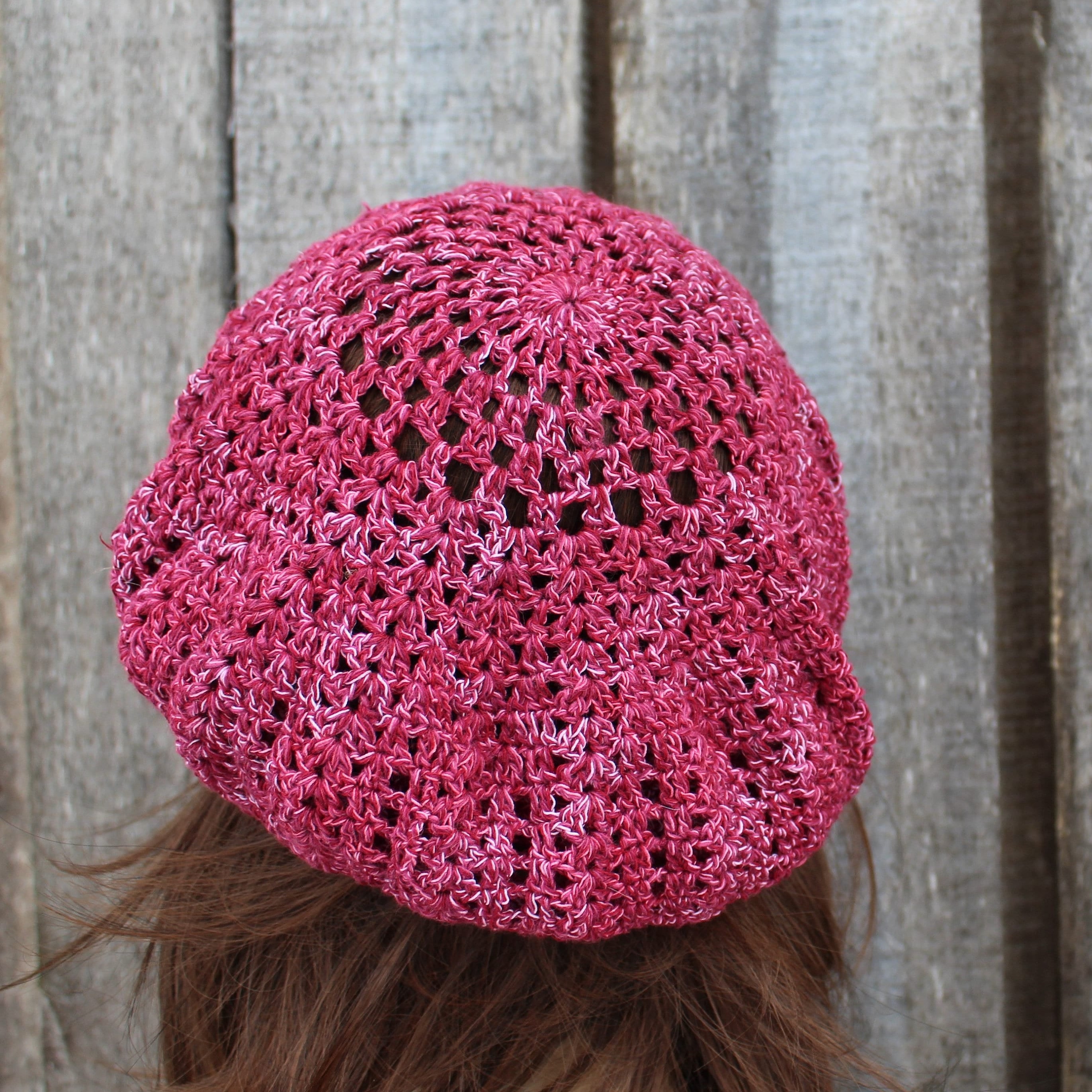 Pink crochet hat worn by a person with wooden planks in the background