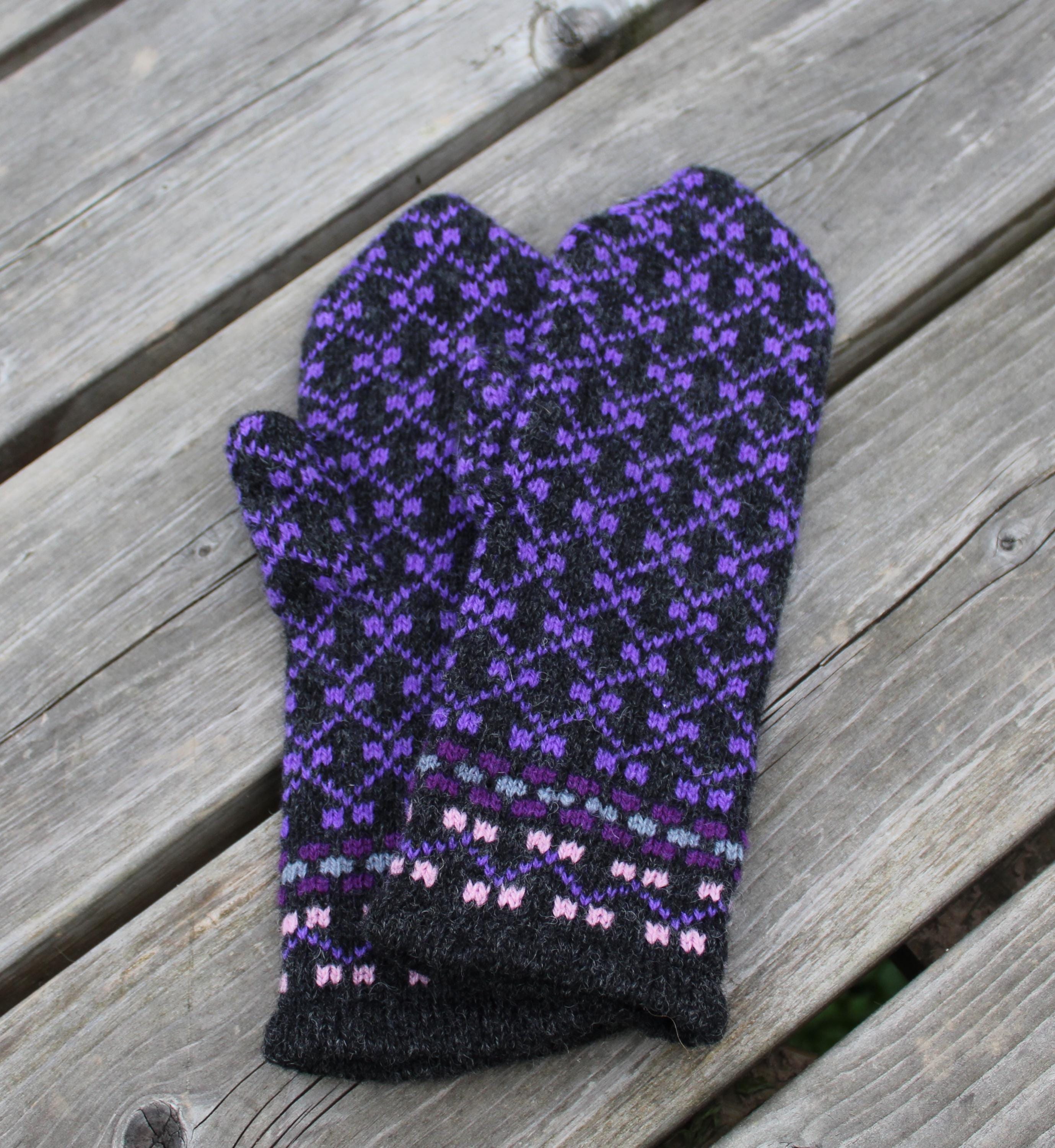 Knitted purple and black patterned mitten on a wooden surface