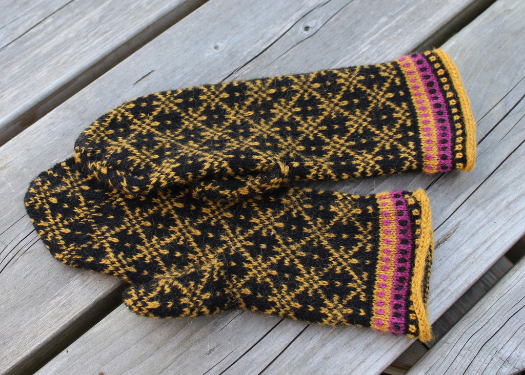 Pair of black and yellow patterned mittens with purple trim on a wooden surface