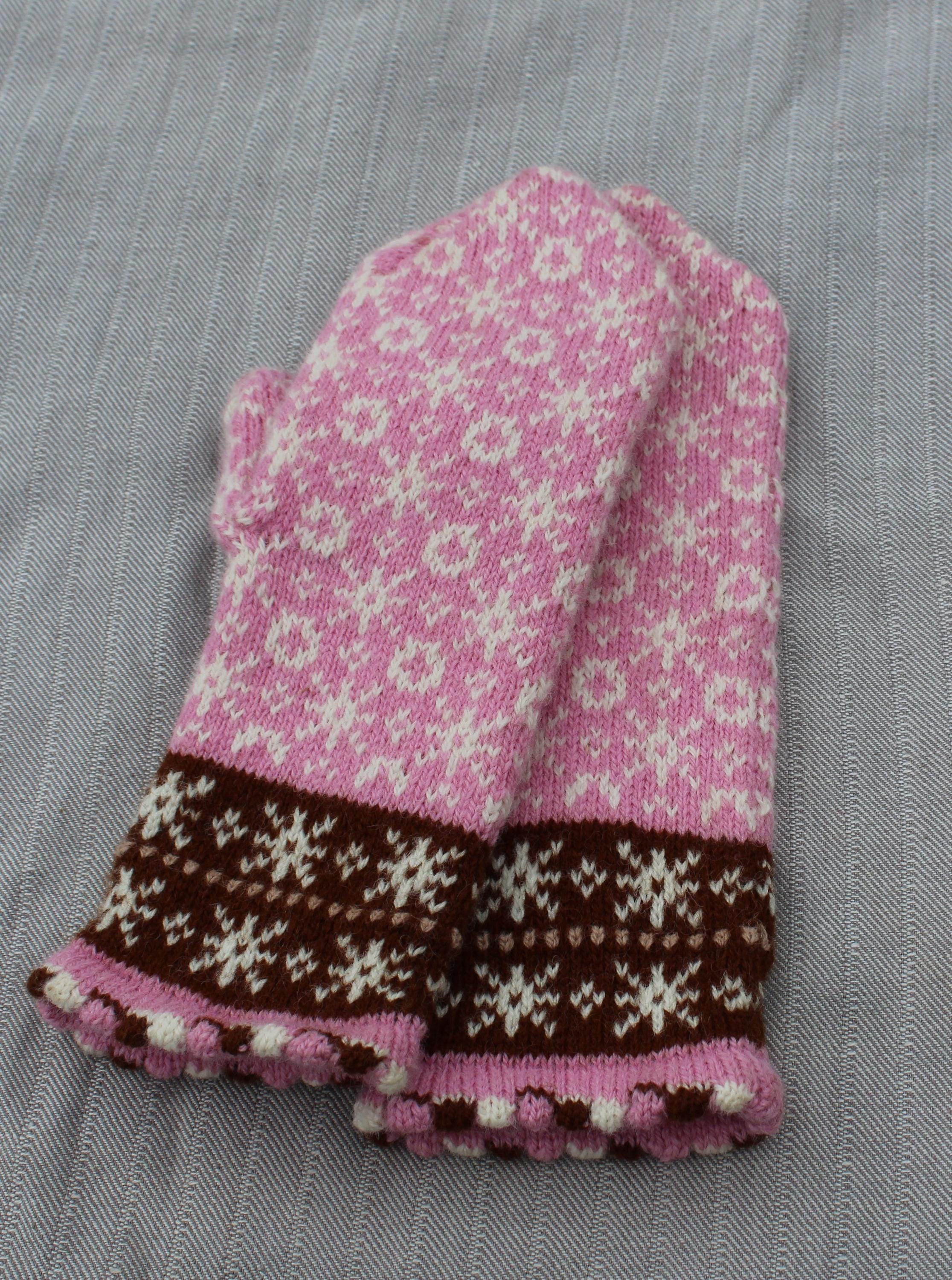 Knitted pink and brown glove on a gray fabric background