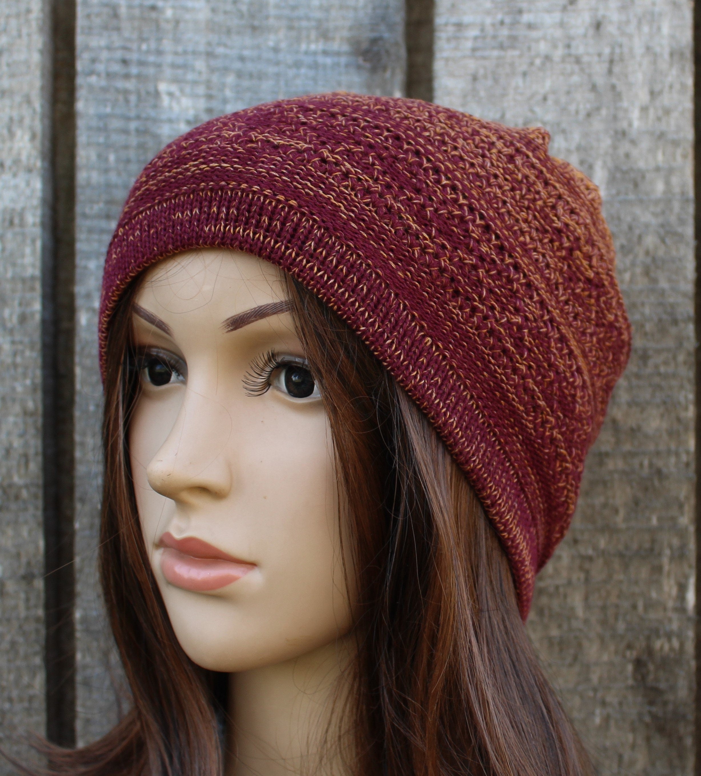 Knitted burgundy beanie on a mannequin head against a wooden background