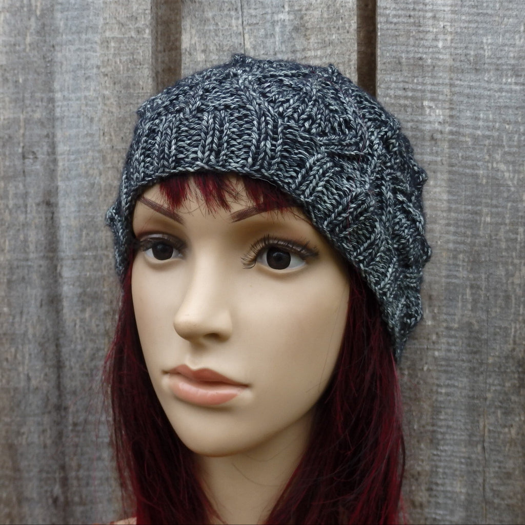 Mannequin head wearing a textured gray knit hat against a wooden background