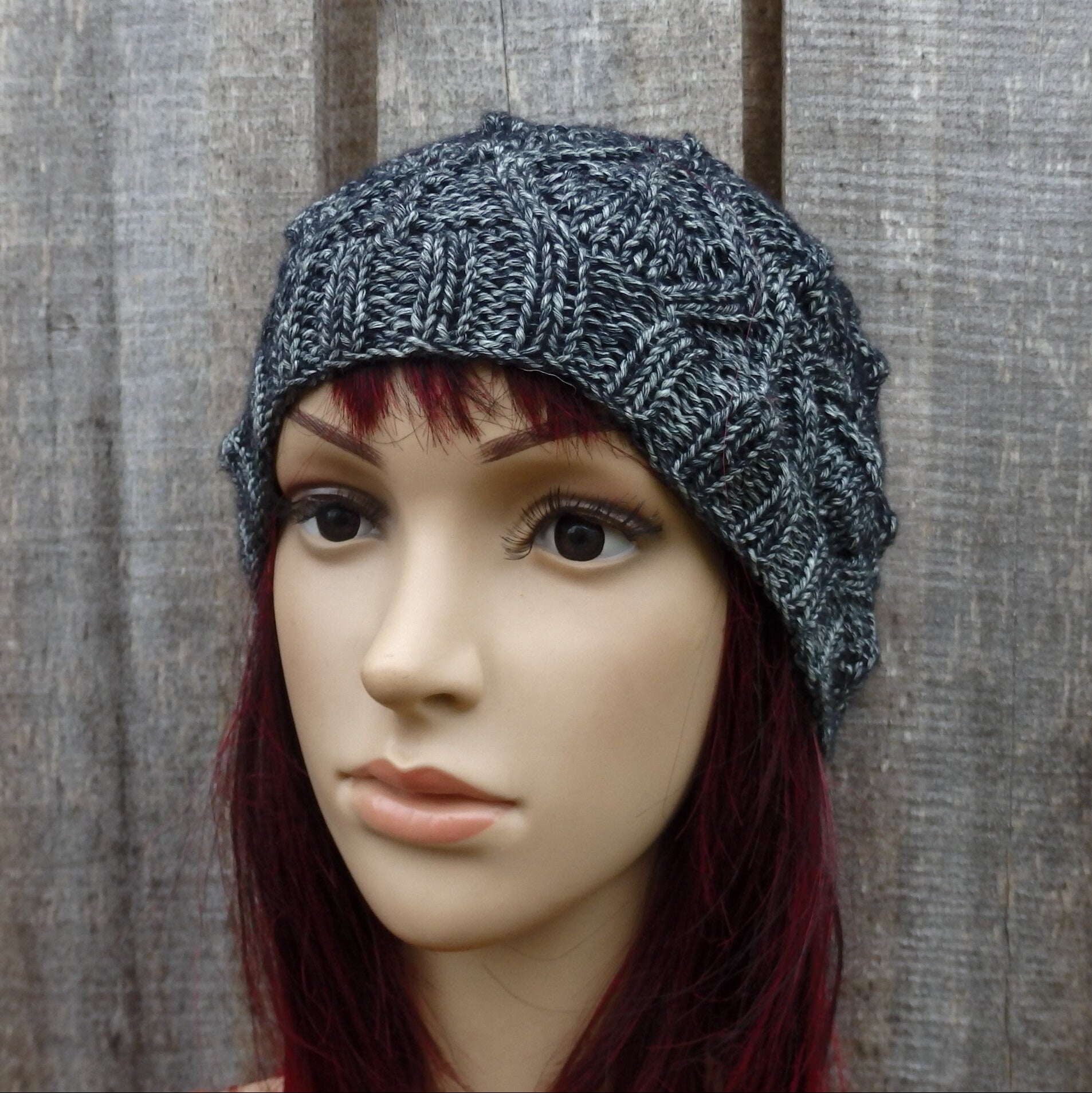 Mannequin head wearing a textured gray knit hat against a wooden background