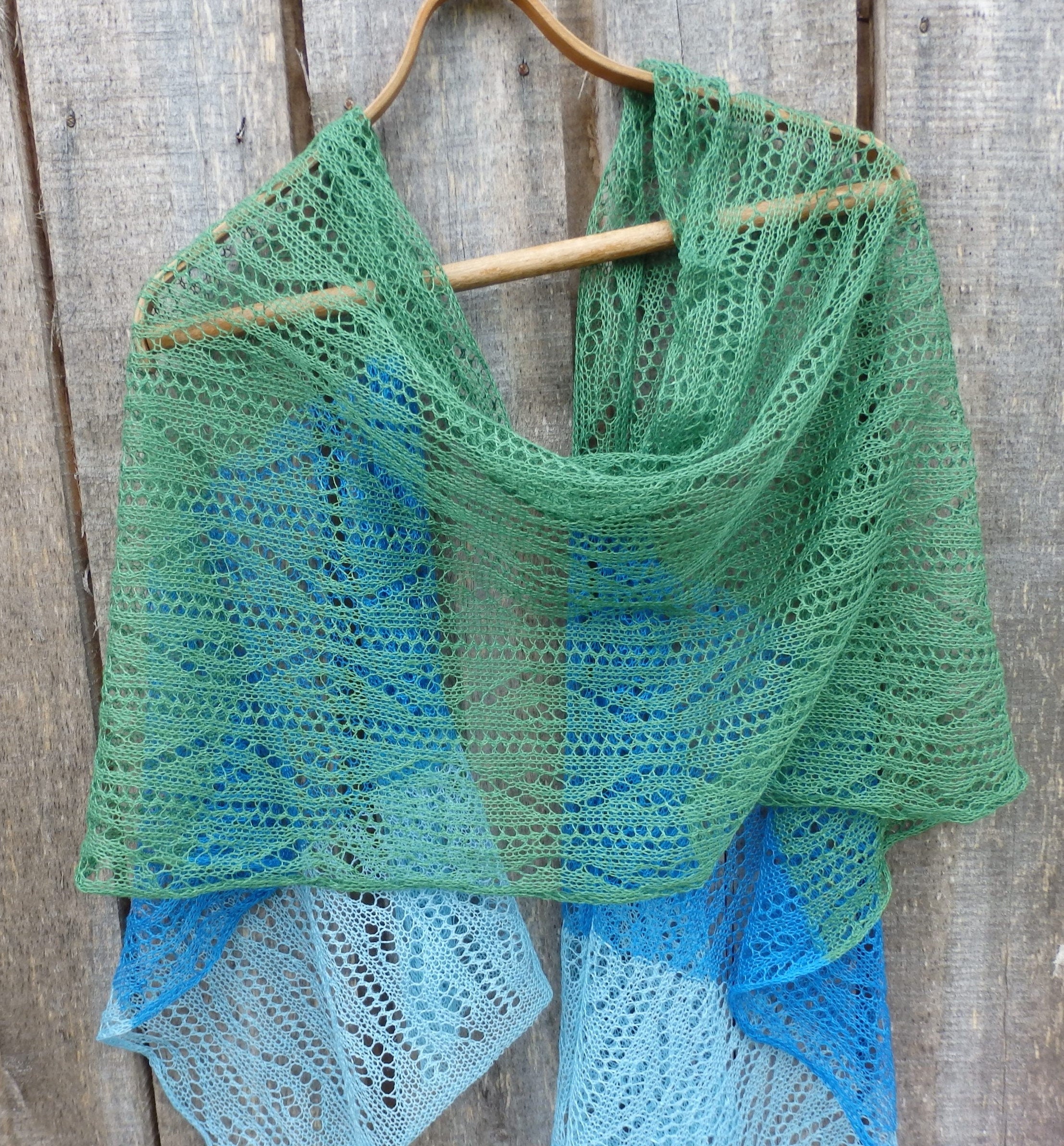 Green and blue knitted shawl on a wooden hanger against a wooden background