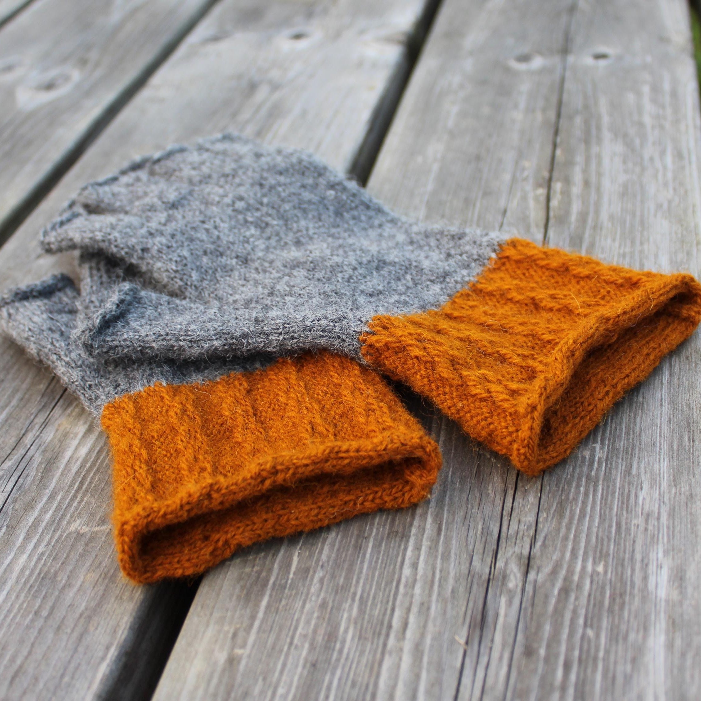 Pair of gray and orange knitted gloves on a wooden surface