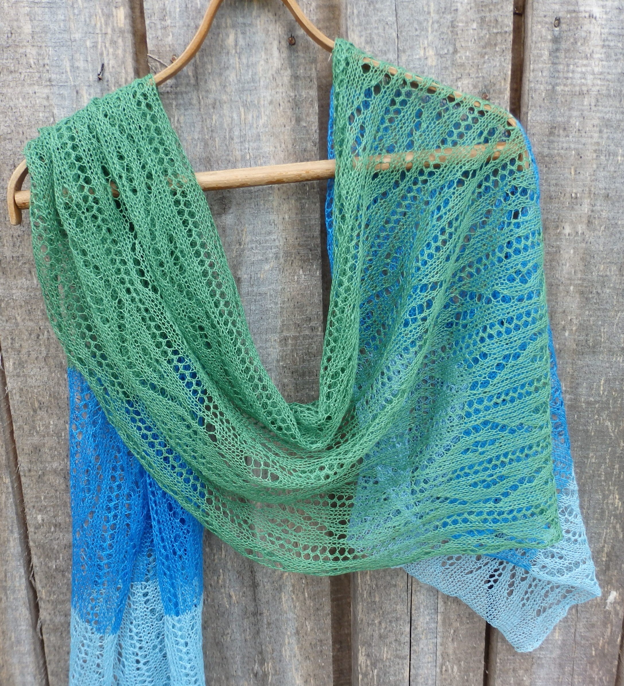 Knitted shawl with green and blue gradient on a wooden background