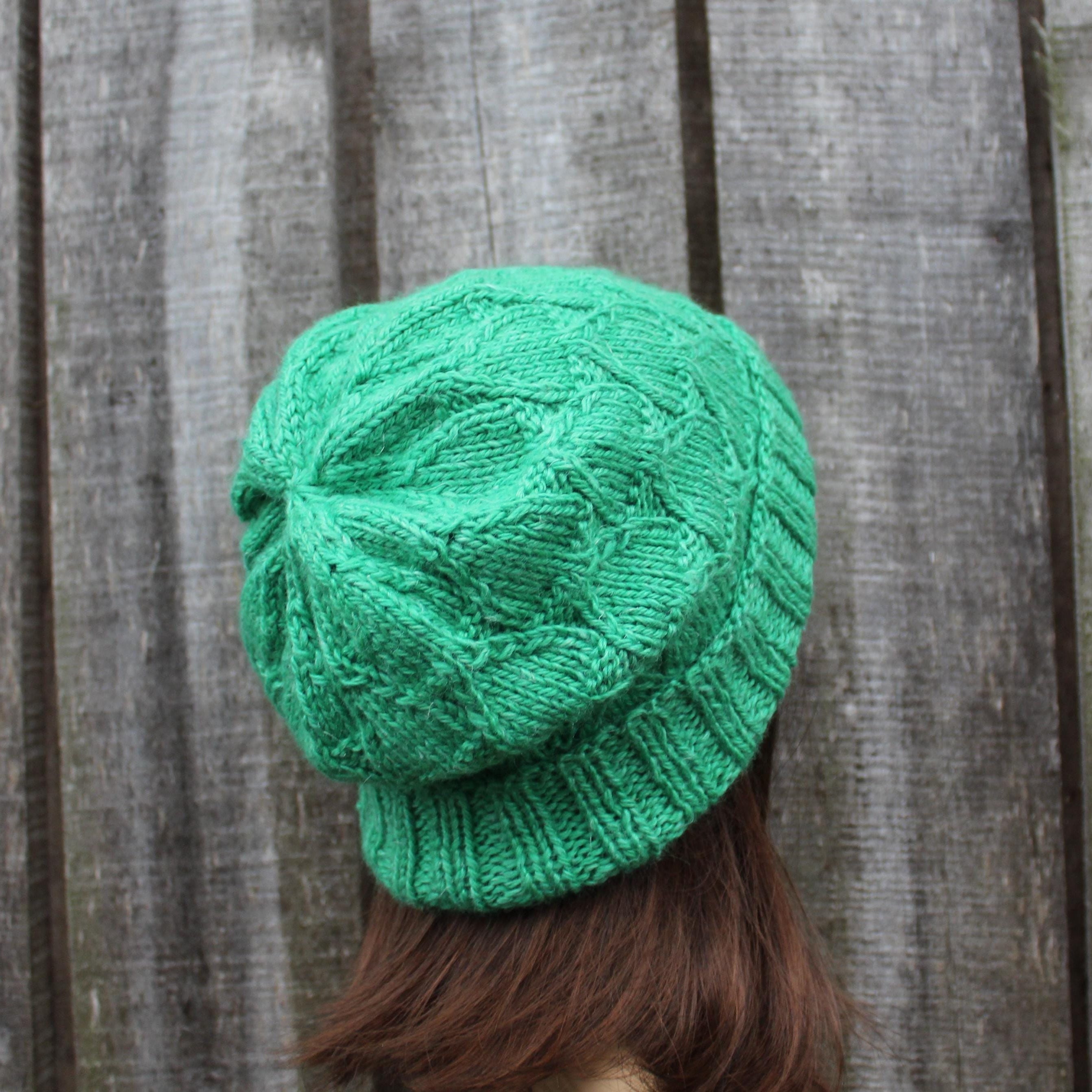 Green knitted beanie worn by a person against a wooden background