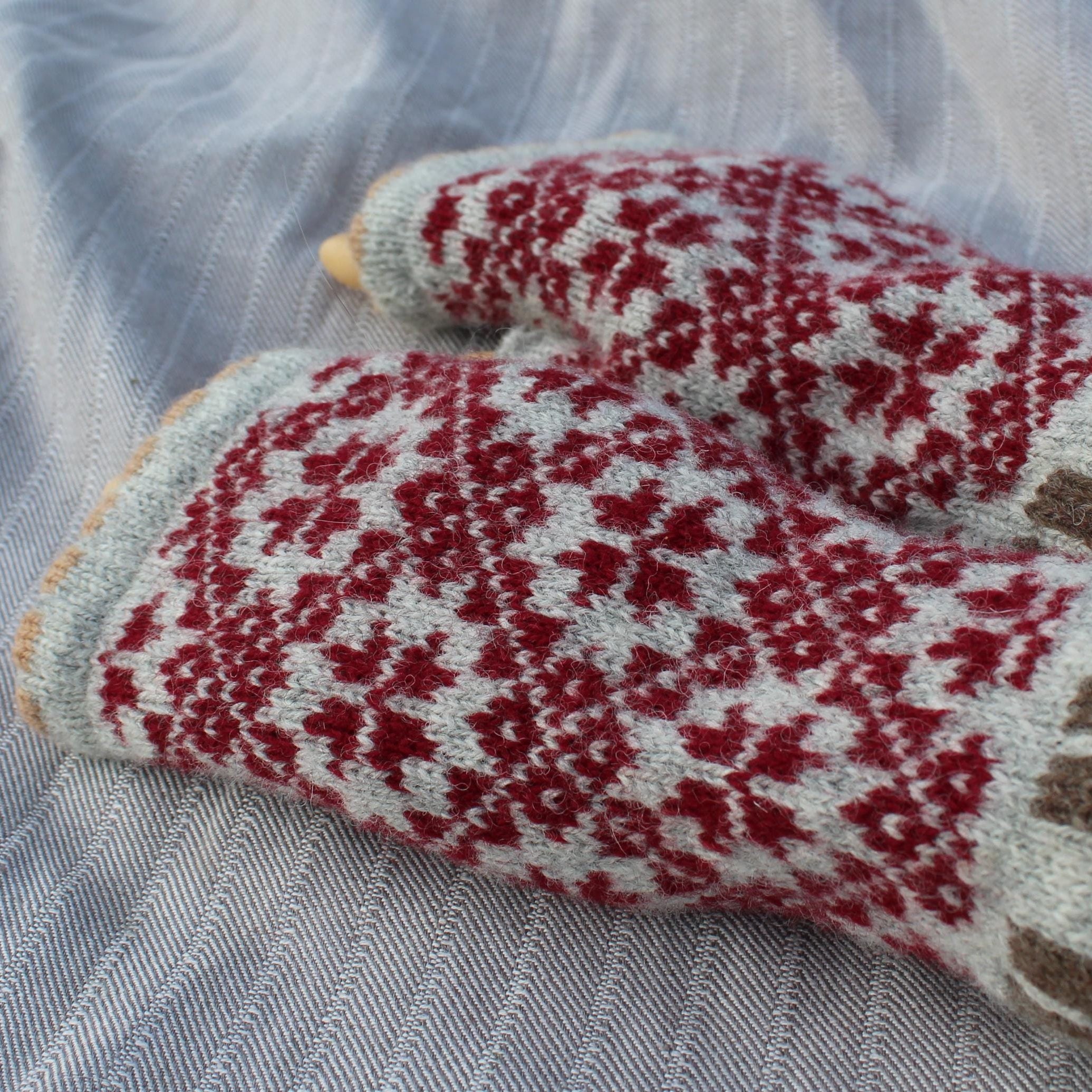 Pair of knitted mittens with red and white pattern on a textured fabric background
