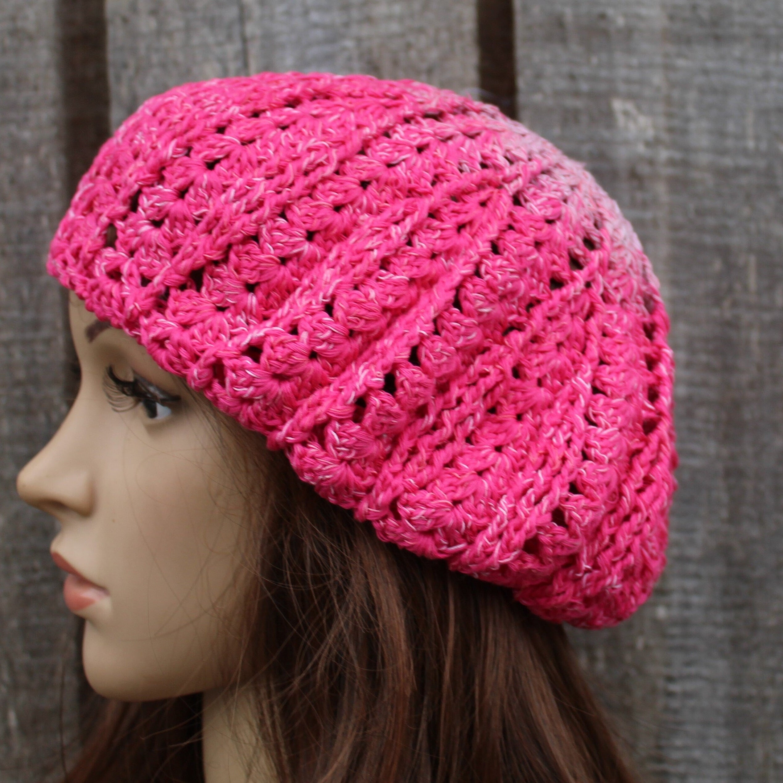 Pink knitted beanie on a mannequin head against a textured brown background