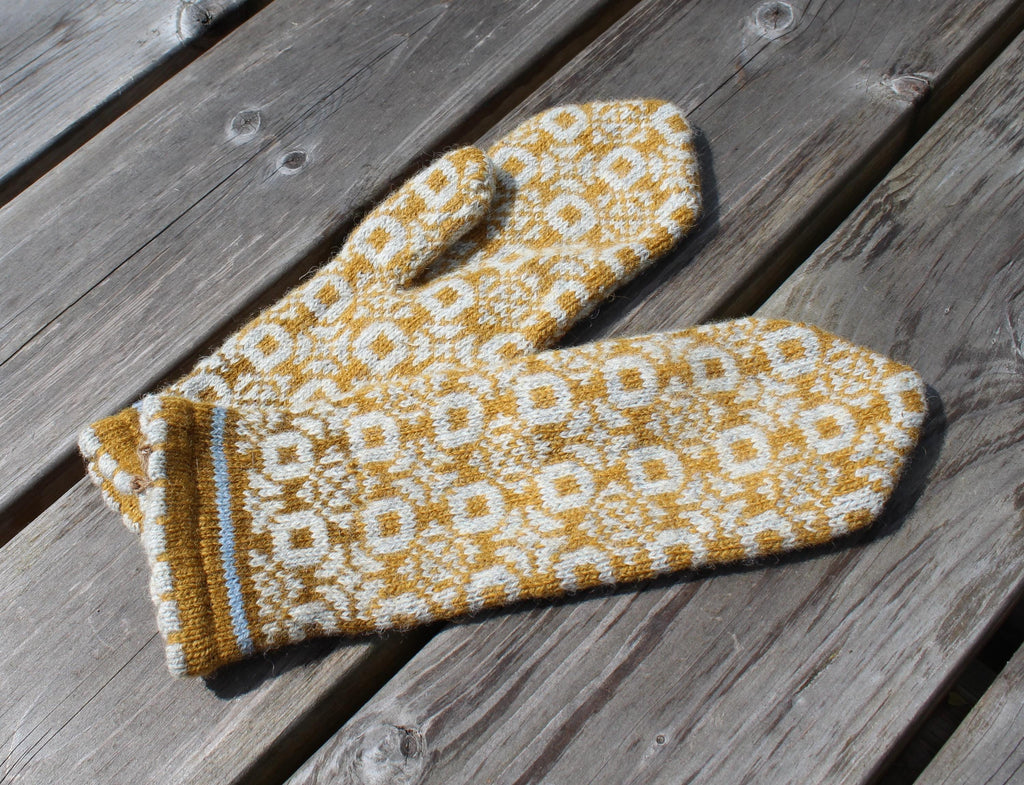 Knitted mittens with a yellow and white pattern on a wooden surface