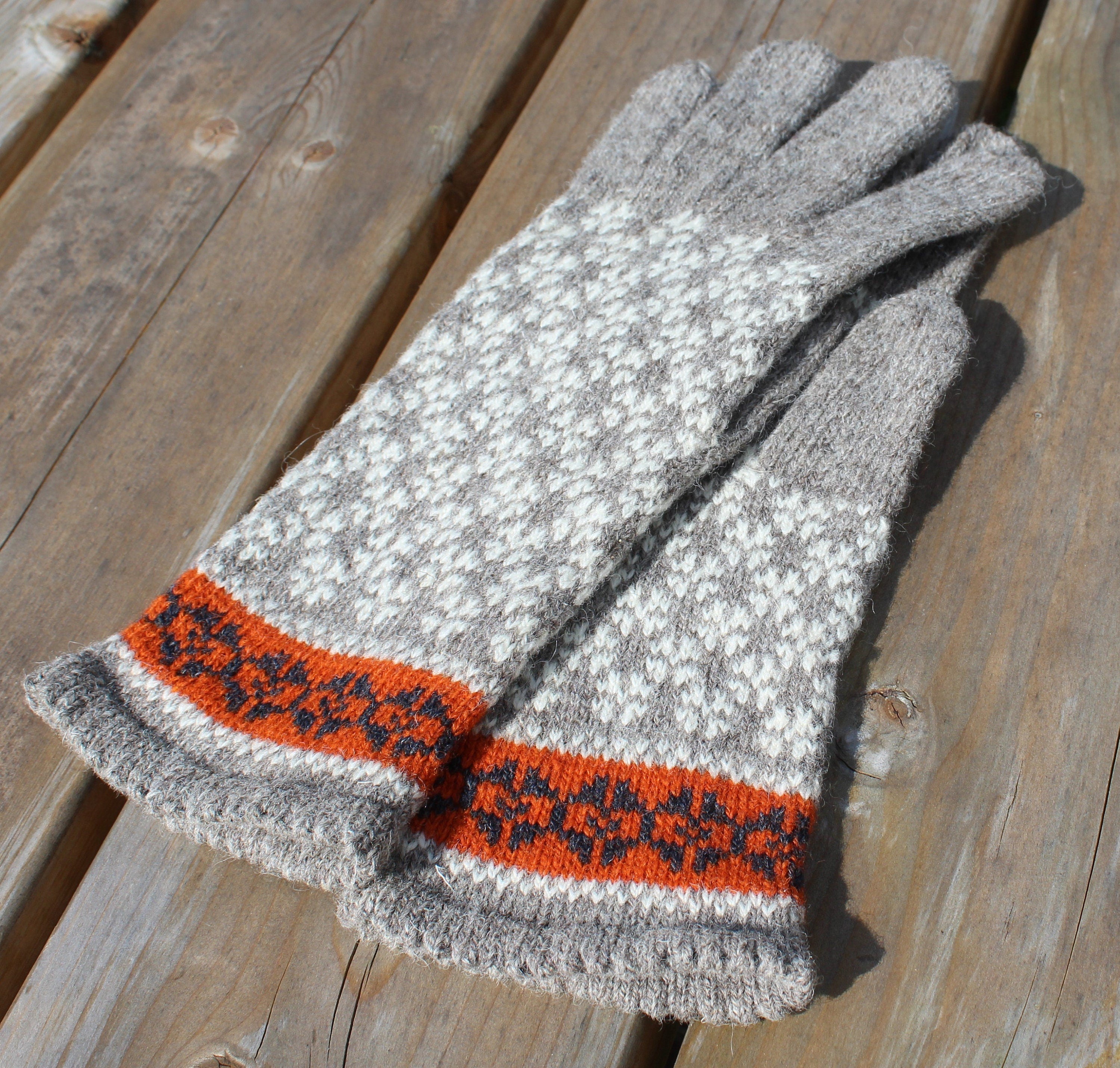 Pair of gray gloves with orange and black pattern on a wooden surface
