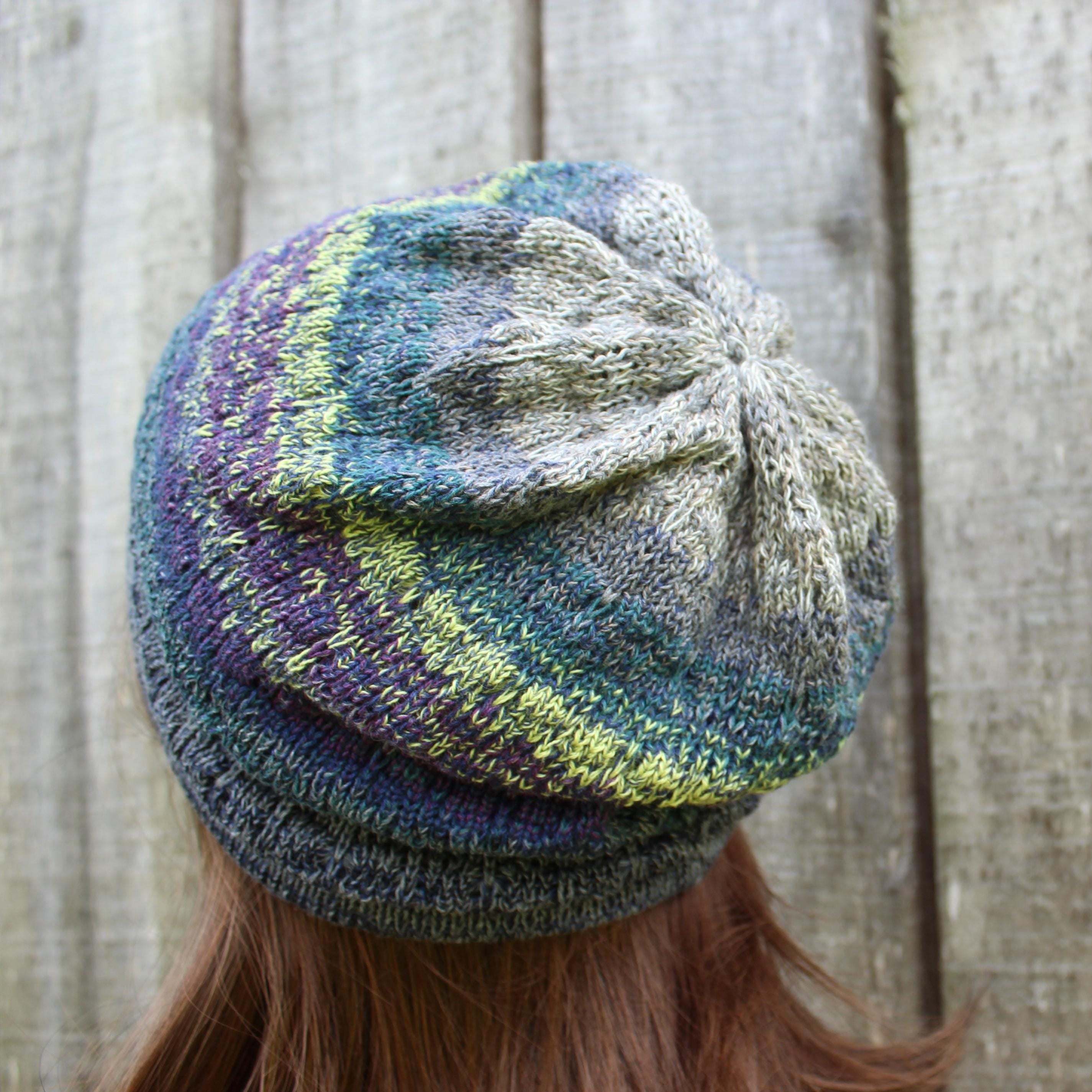 Multicolored knitted beanie worn by a person with a wooden background