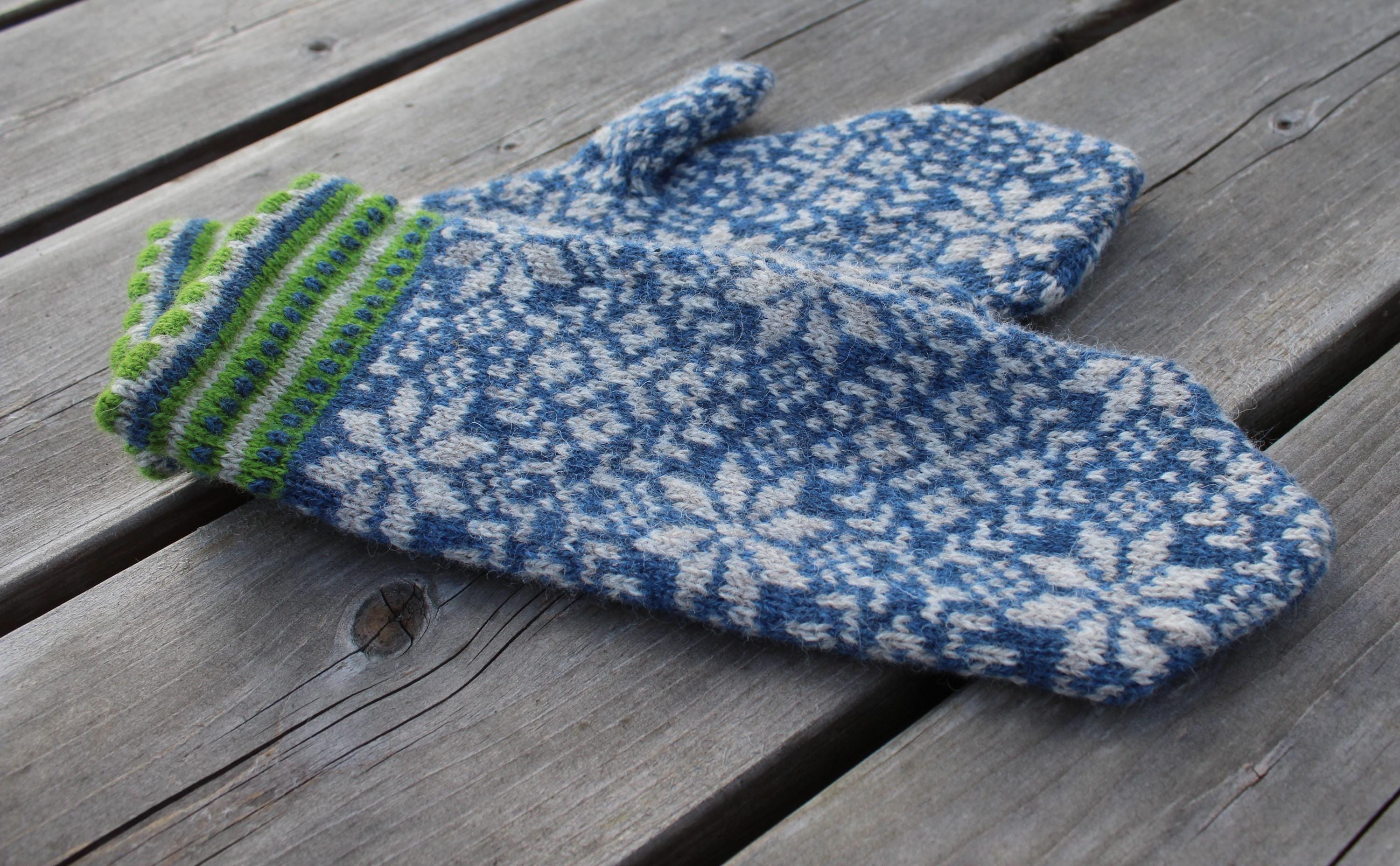 Pair of blue and white patterned mittens with green cuffs on a wooden surface