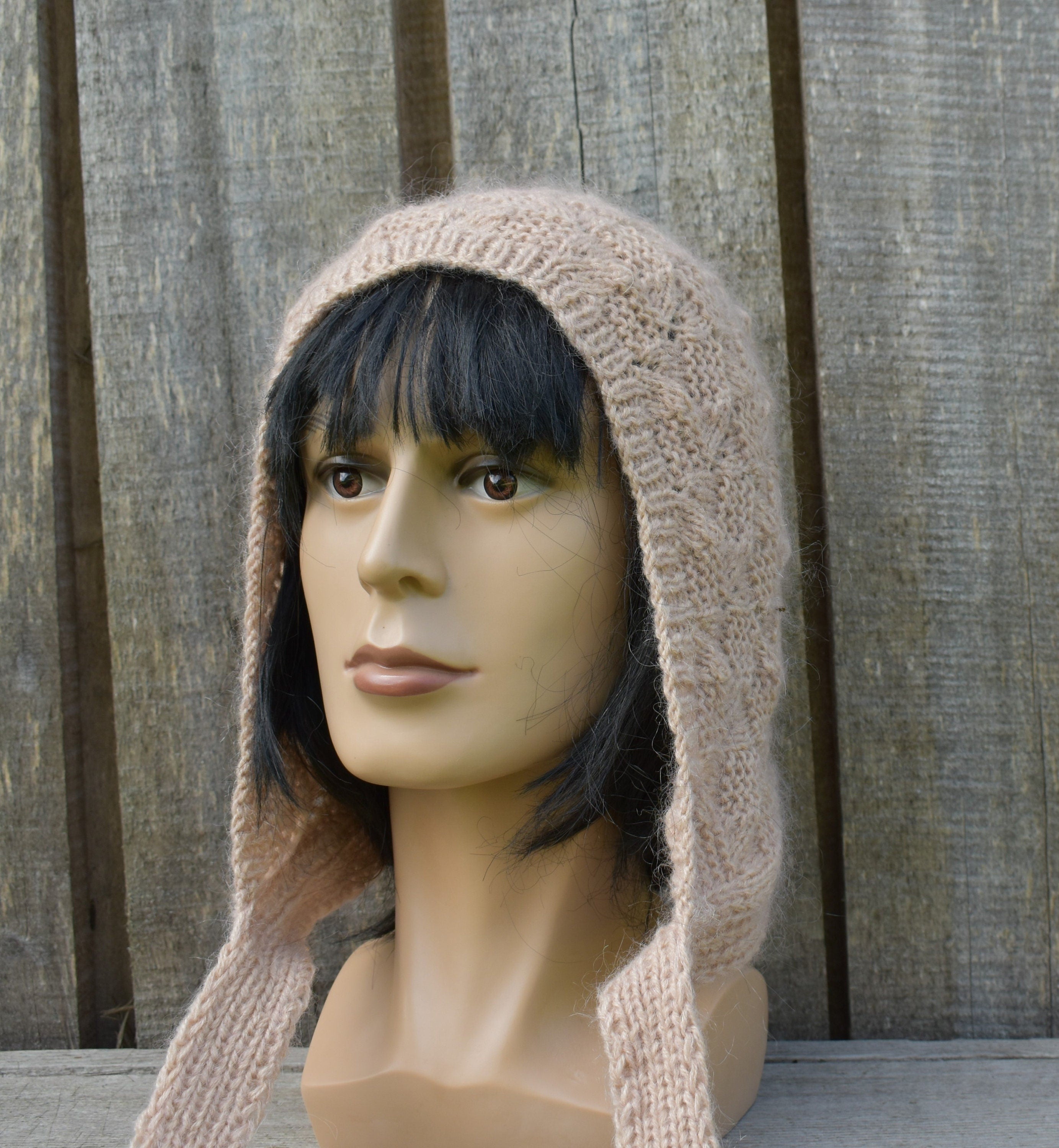 Mannequin head wearing a beige knitted hood against a wooden background