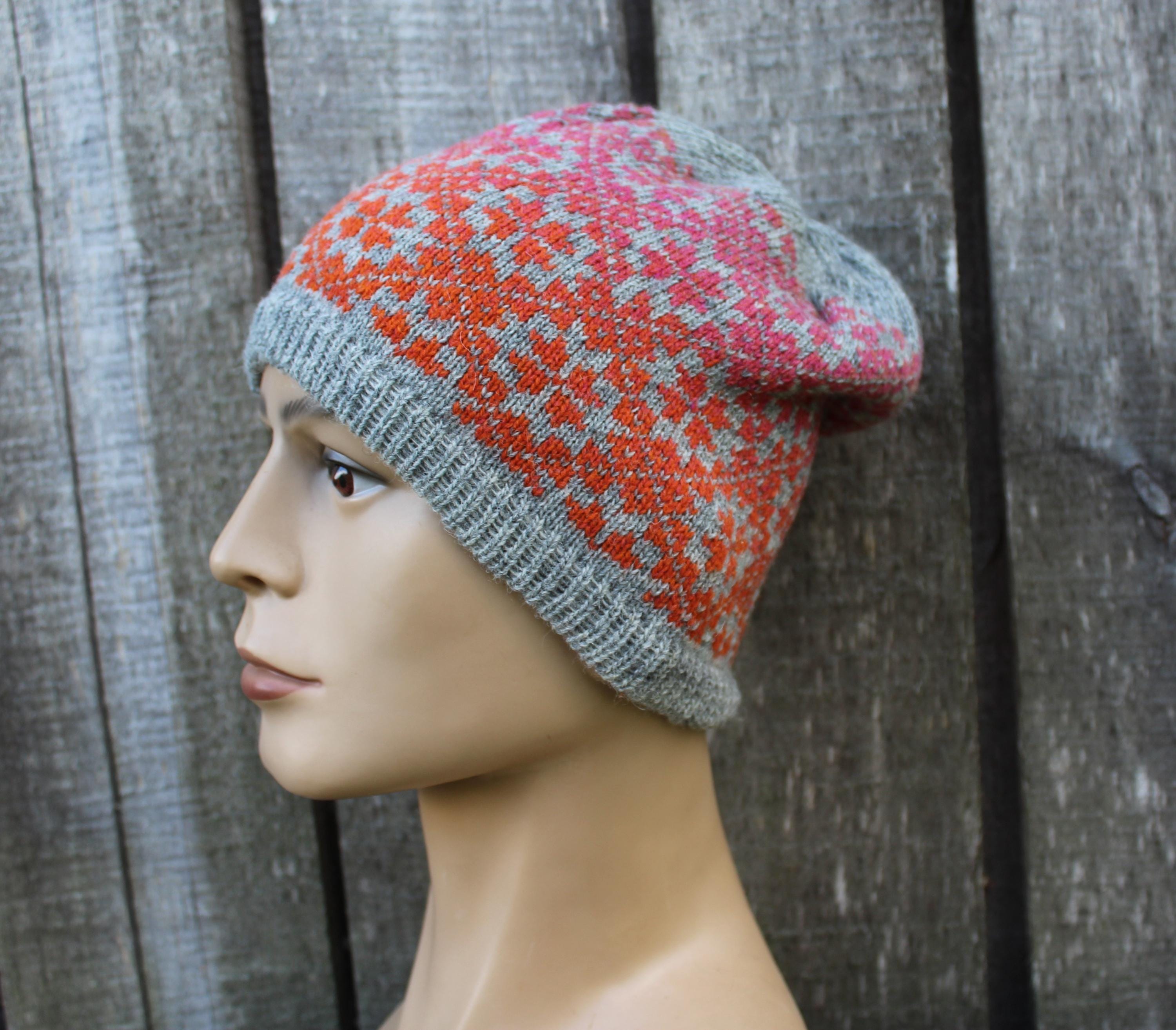Mannequin head wearing a colorful knitted beanie against a wooden background
