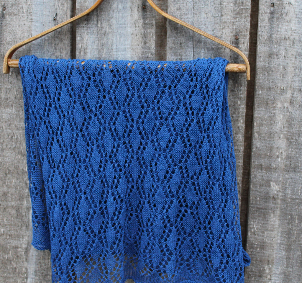 Blue knitted shawl on a wooden hanger against a rustic wooden background