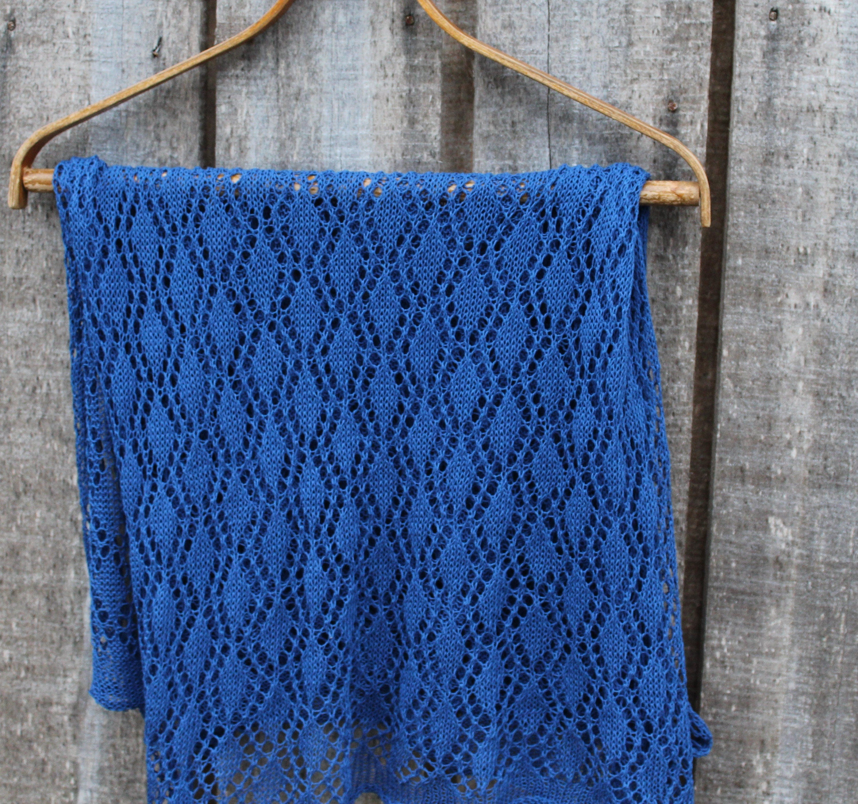Blue knitted shawl on a wooden hanger against a rustic wooden background