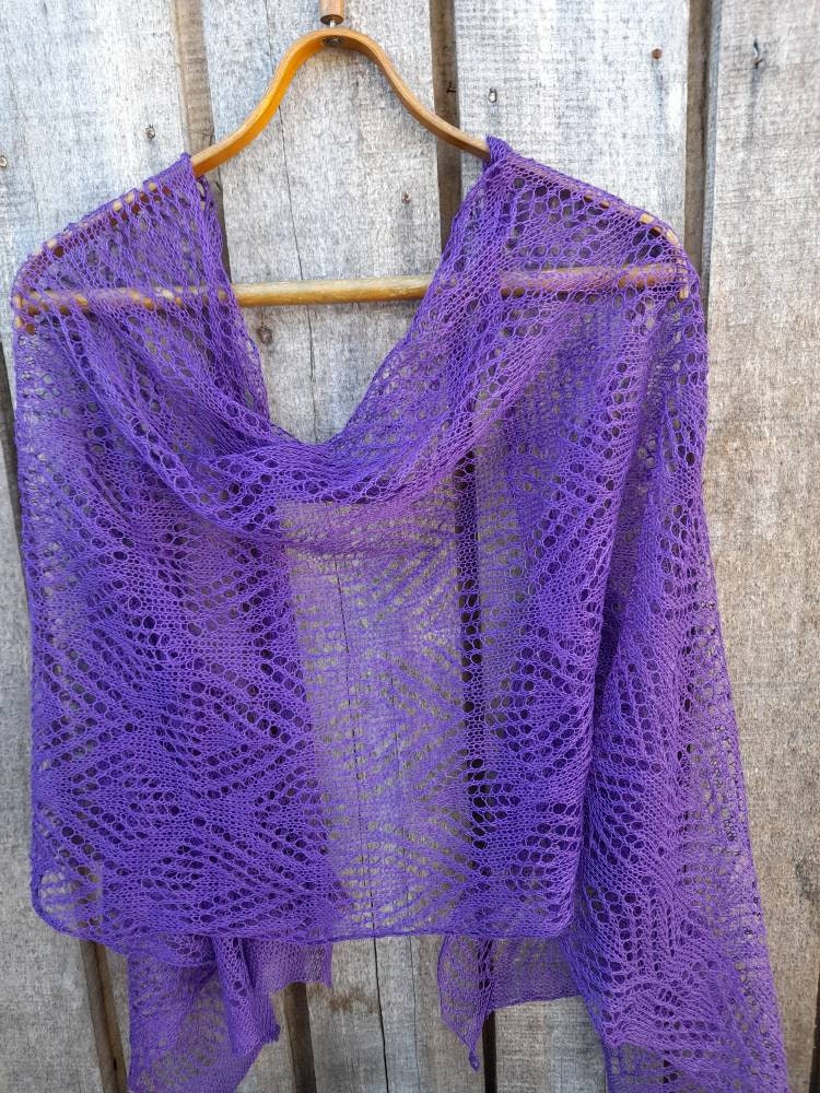 Purple knitted shawl on a wooden hanger against a rustic wooden background