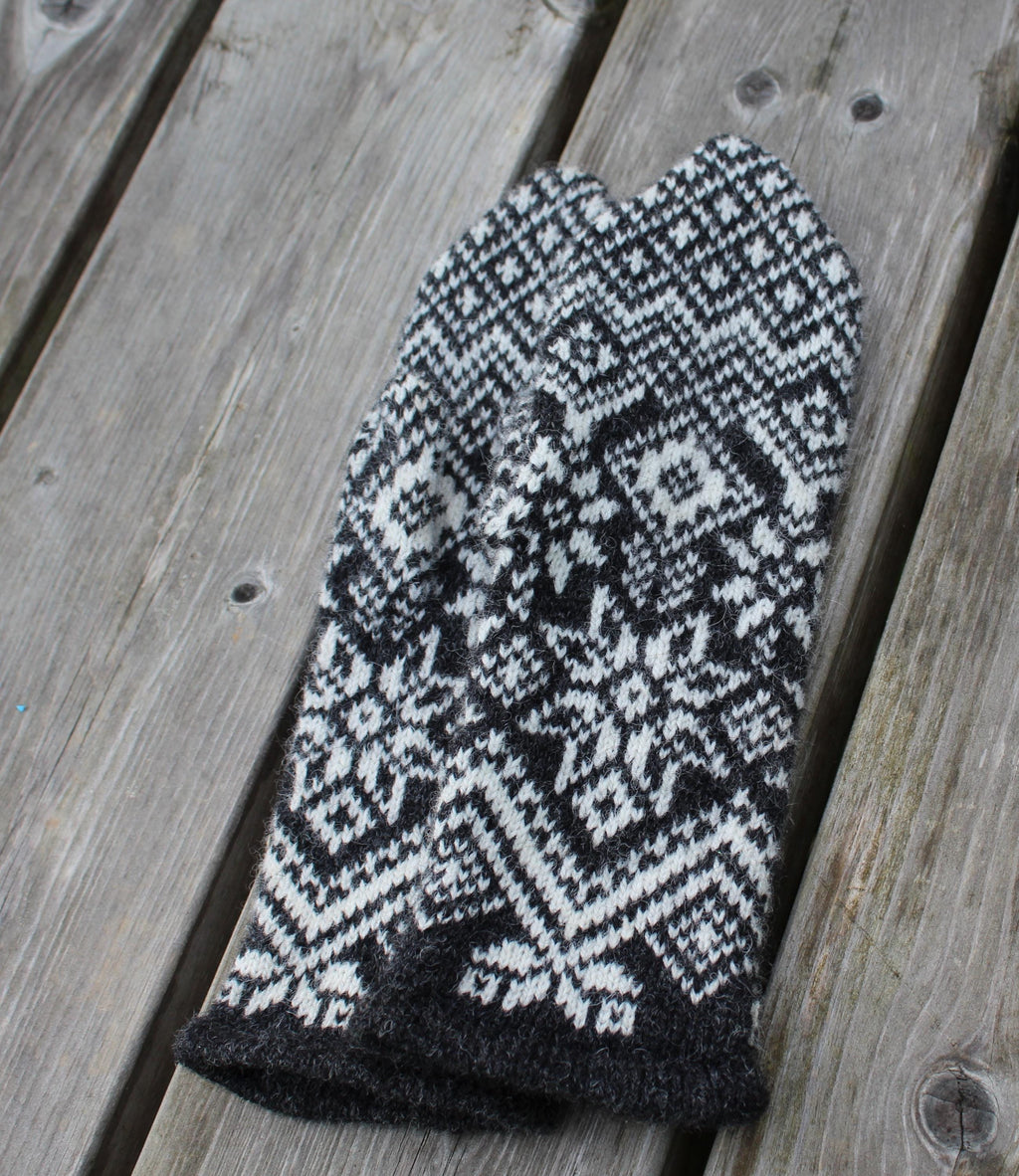 Knitted black and white patterned mitten on a wooden surface