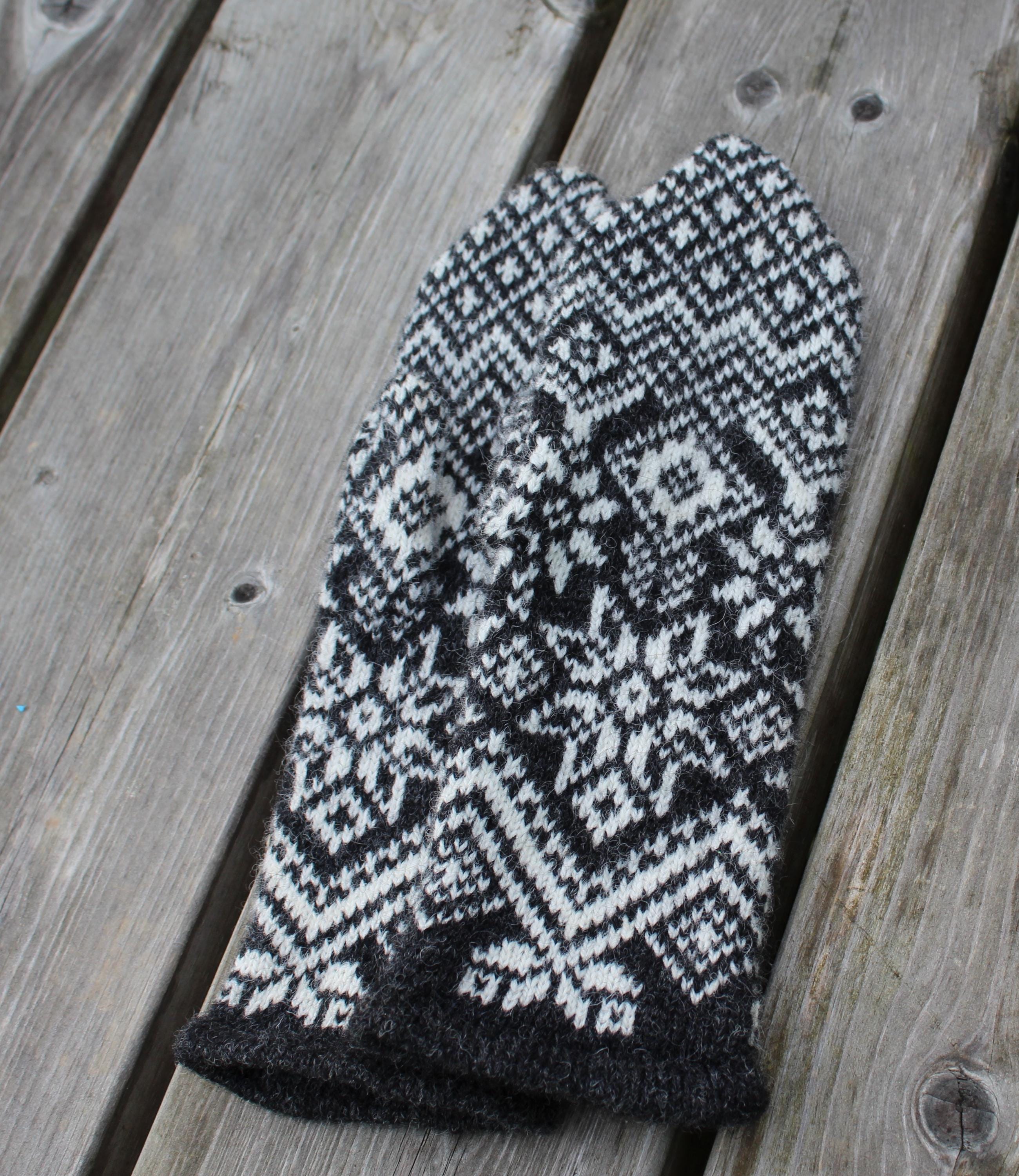 Knitted black and white patterned mitten on a wooden surface
