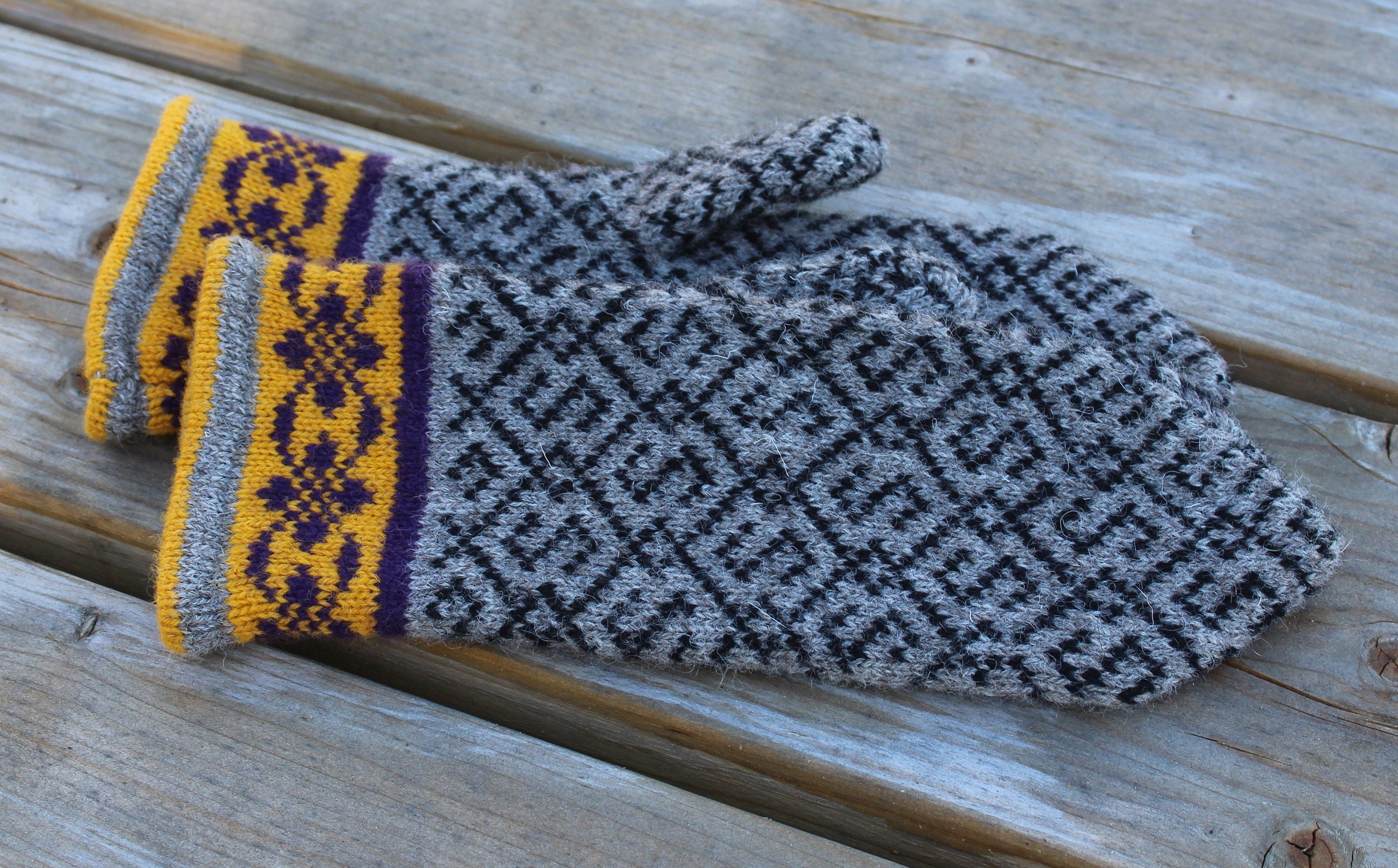 Pair of gray and yellow patterned mittens on a wooden surface