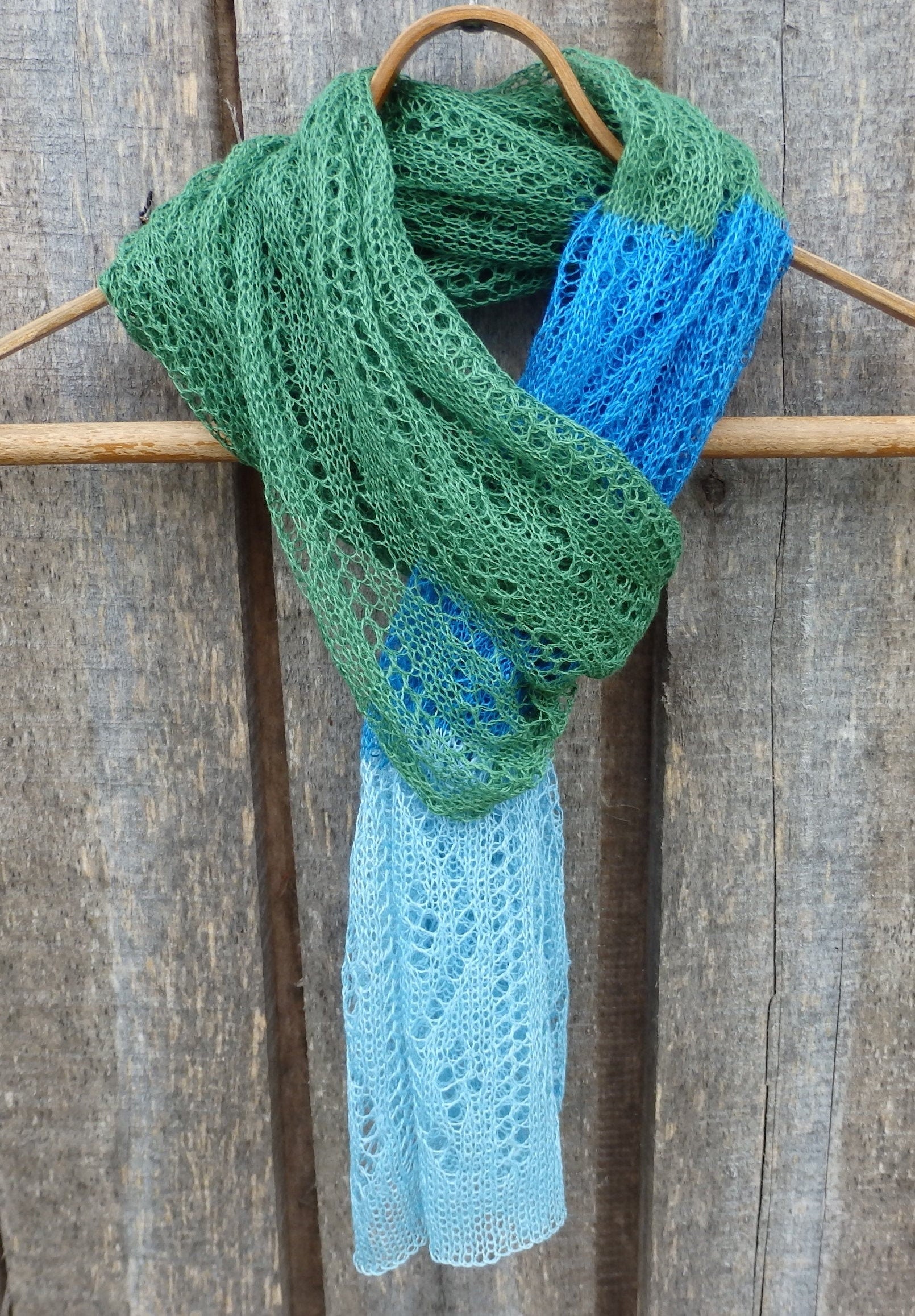 Knitted scarf with green and blue pattern draped over a wooden surface