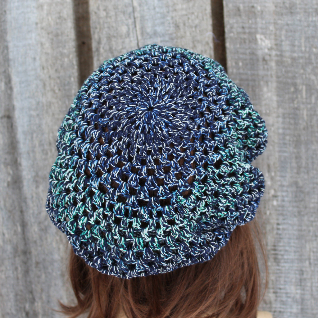 Blue and green crocheted beanie worn by a person against a wooden background