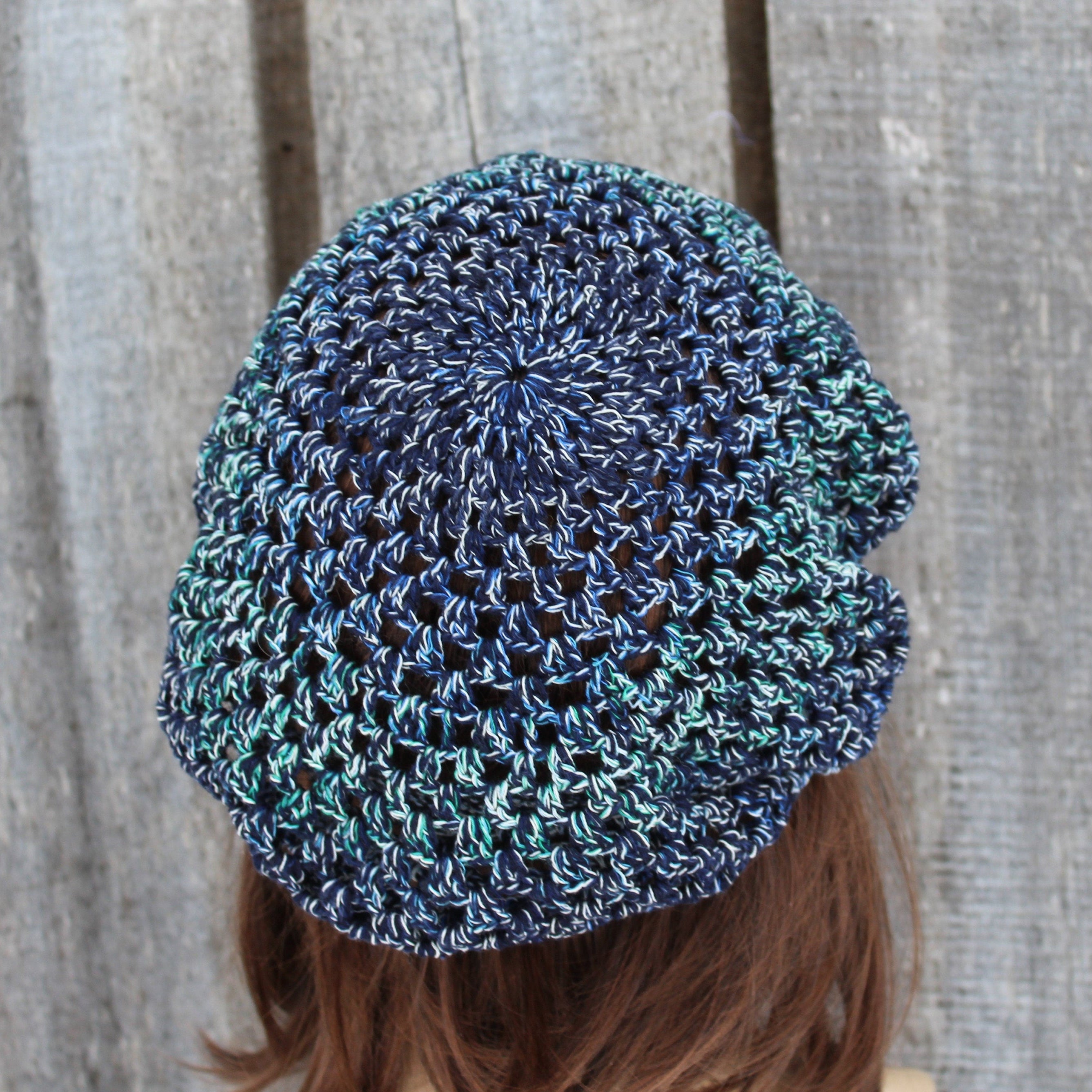 Blue and green crocheted beanie worn by a person against a wooden background