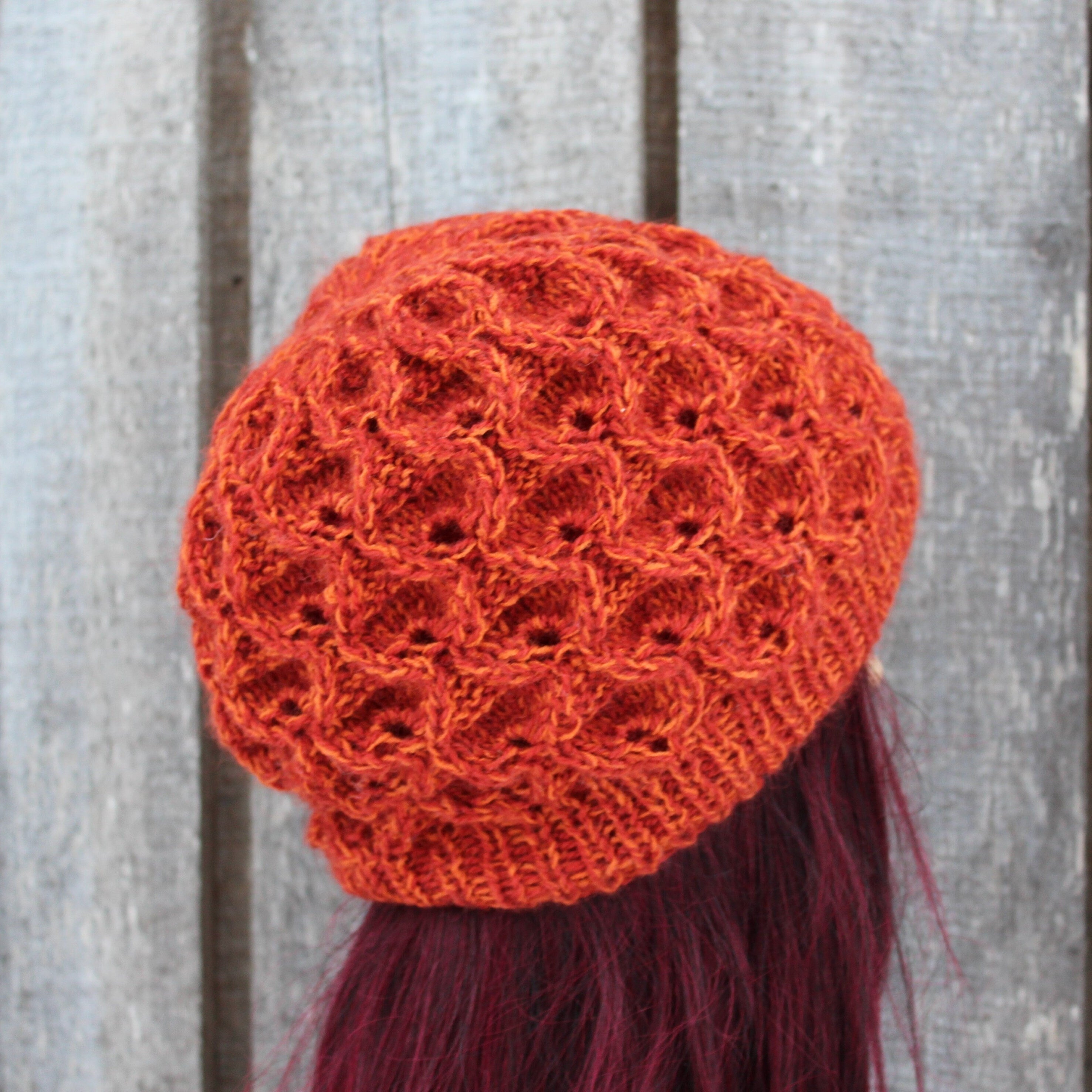 Orange knitted hat on a mannequin head against a wooden background