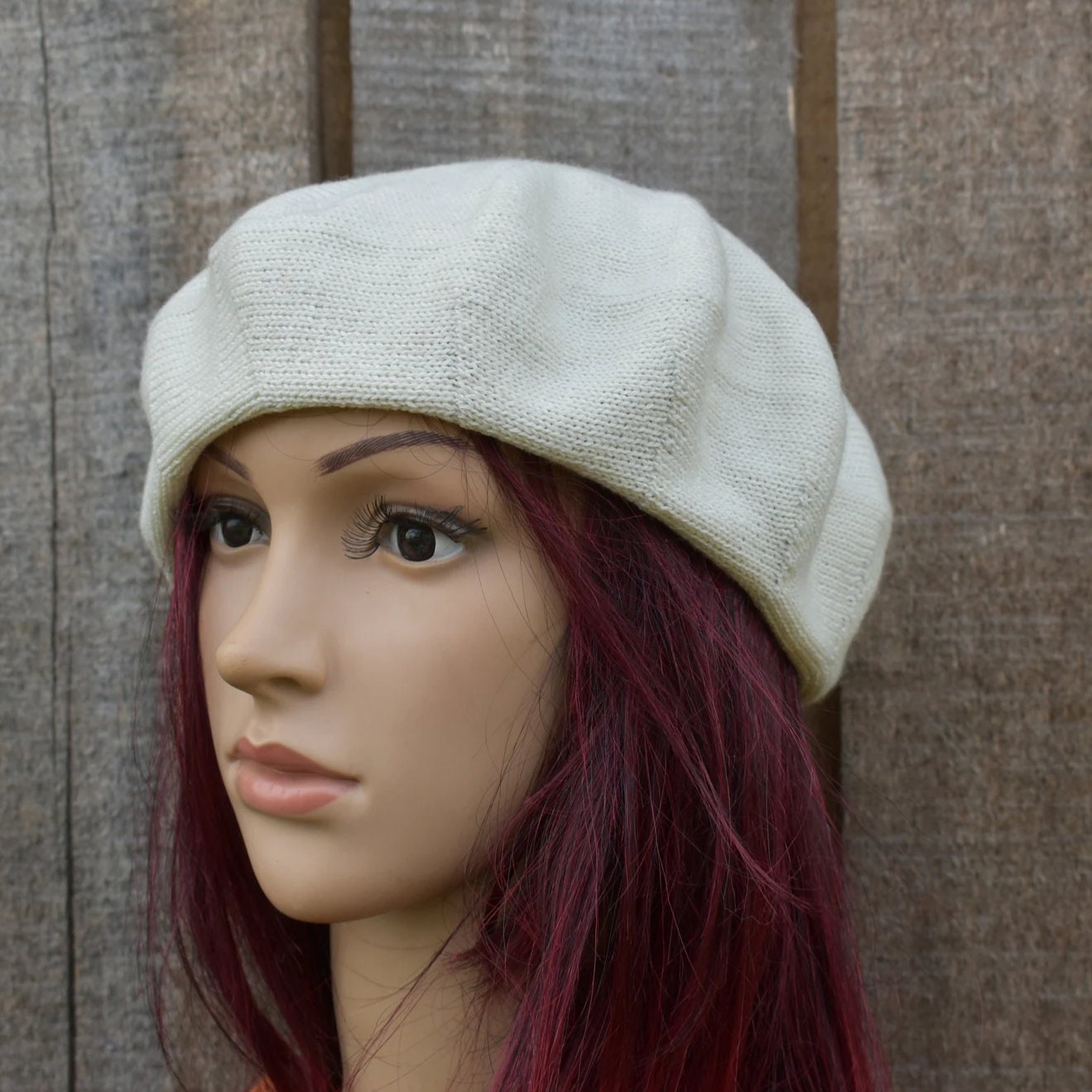 Mannequin head wearing a beige beret against a wooden background
