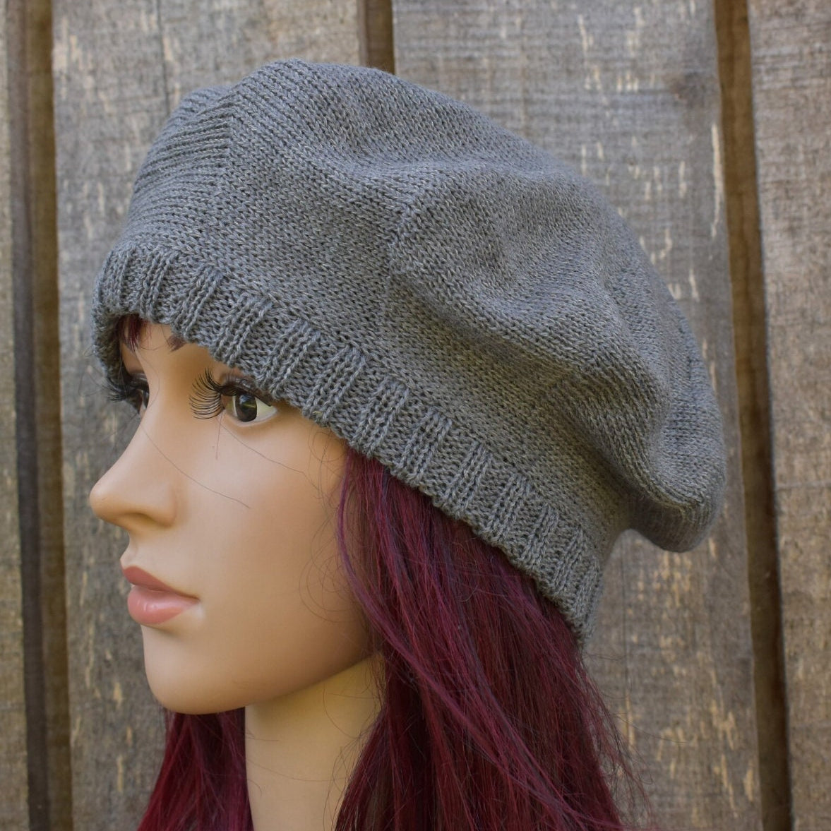 Gray knit beret worn by a mannequin against a wooden background