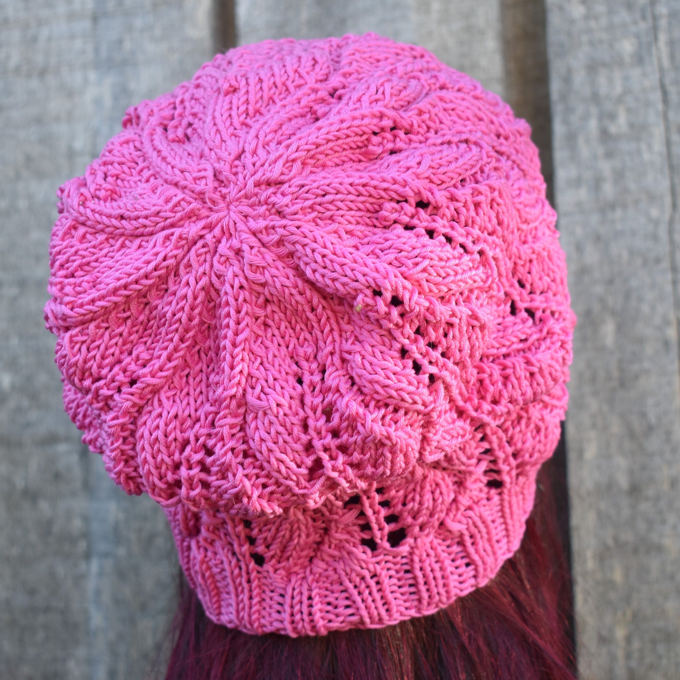 Pink knitted beanie on a person with red hair against a wooden background