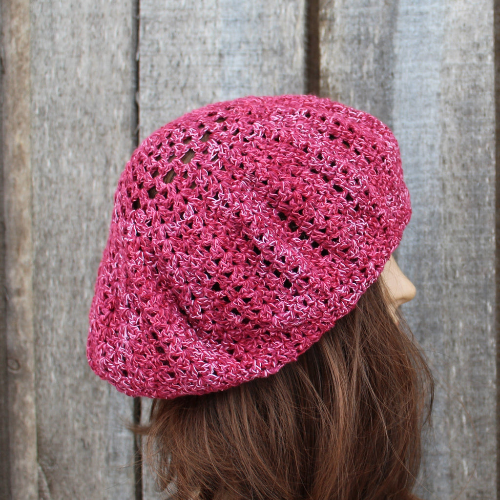 Pink crocheted beret worn by a person against a wooden background