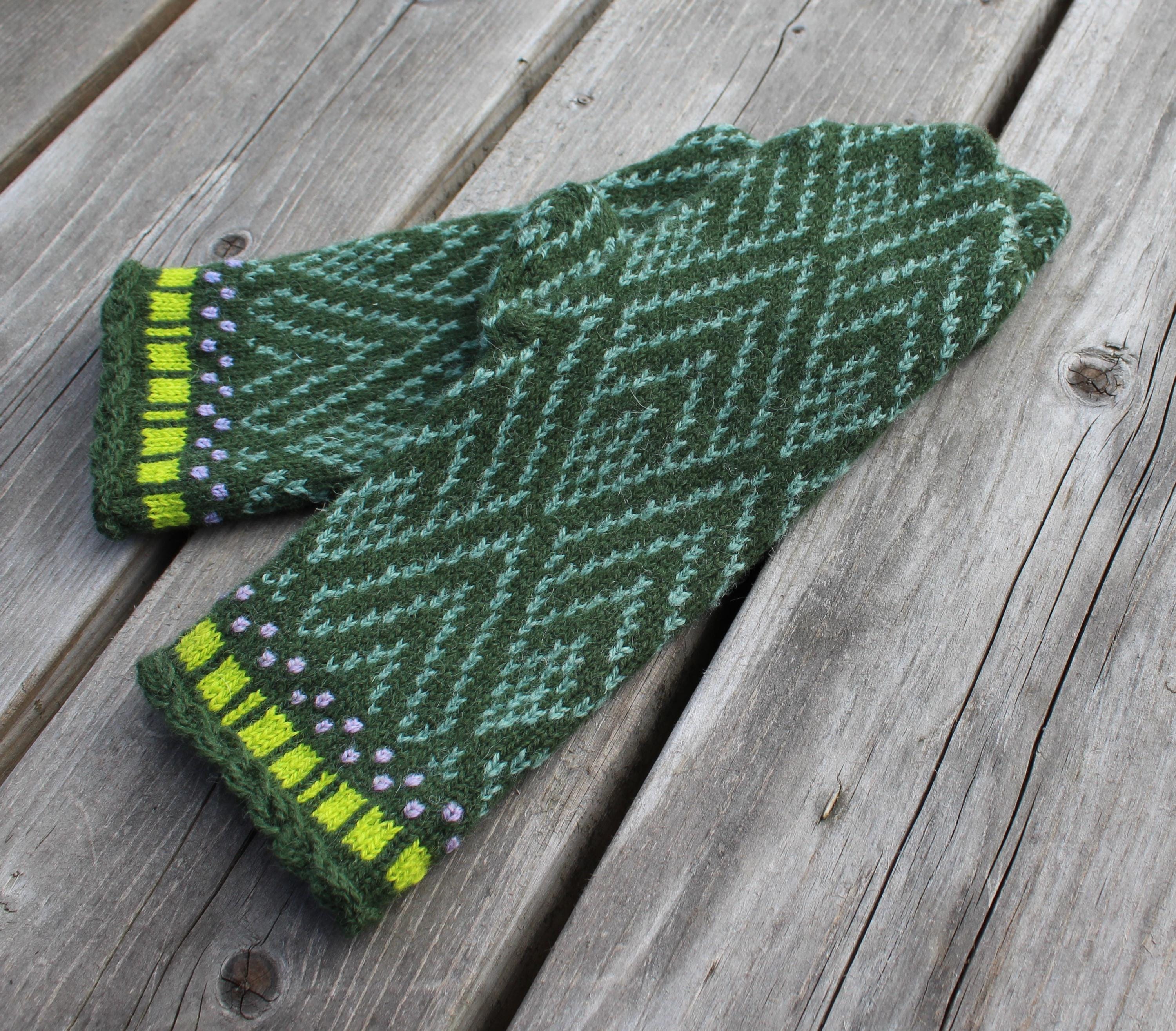 Green knitted mittens with a pattern on a wooden surface
