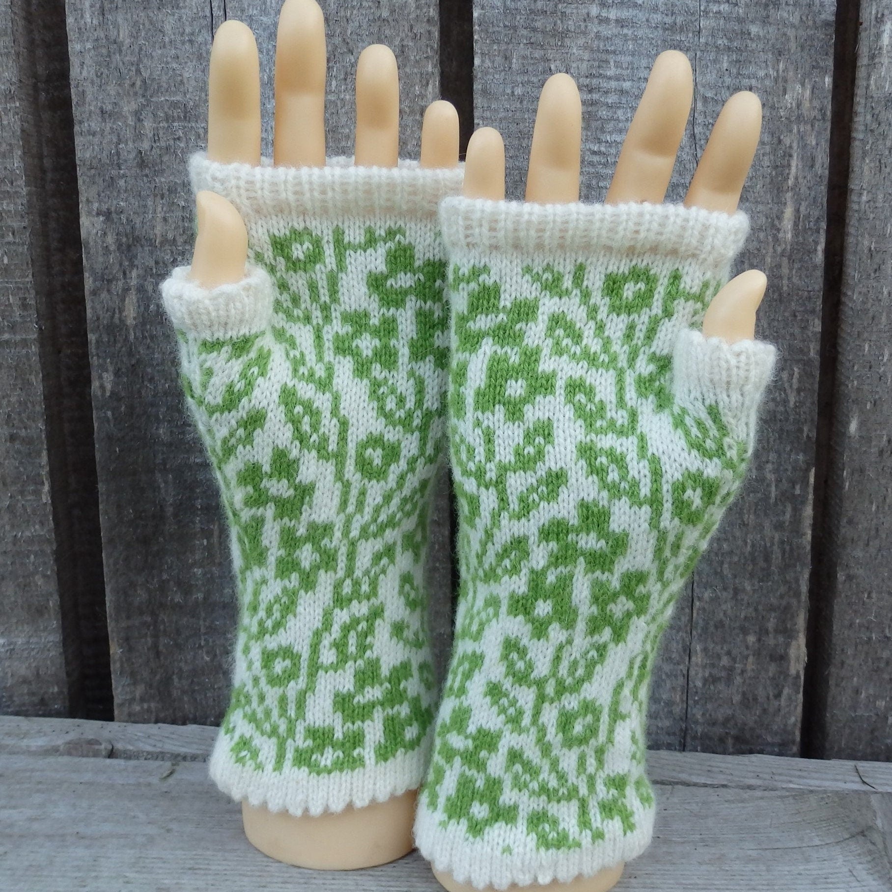 Green and white patterned fingerless gloves on a mannequin hand against a wooden background