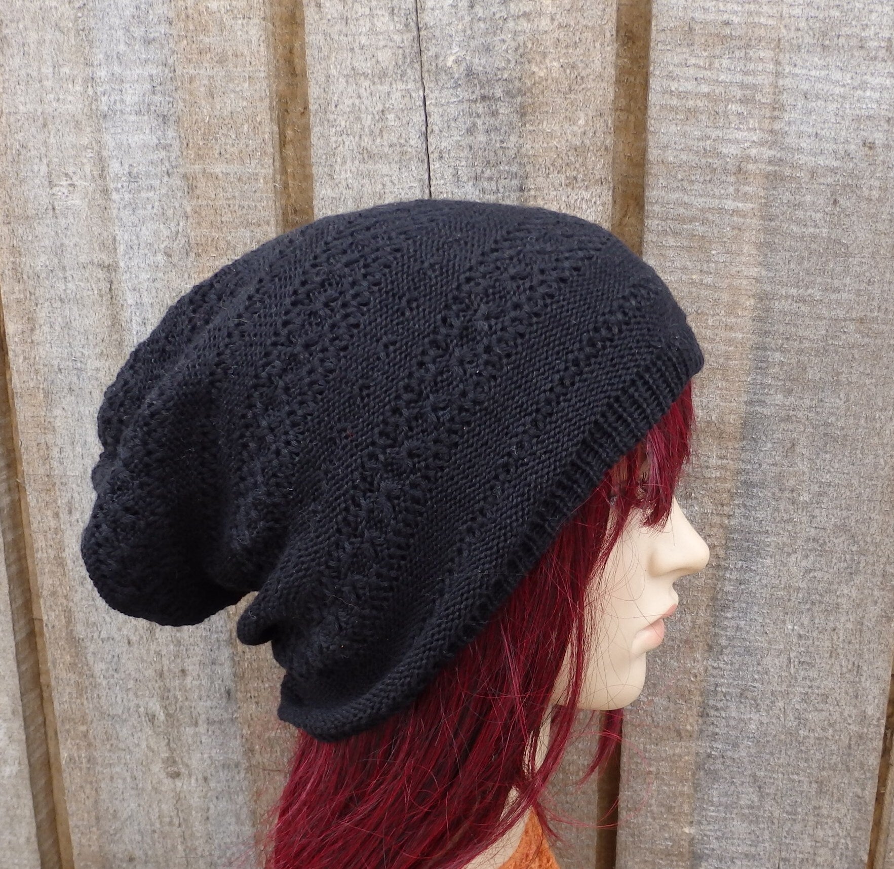 Black knitted hat on a mannequin head with red hair against a wooden panel background