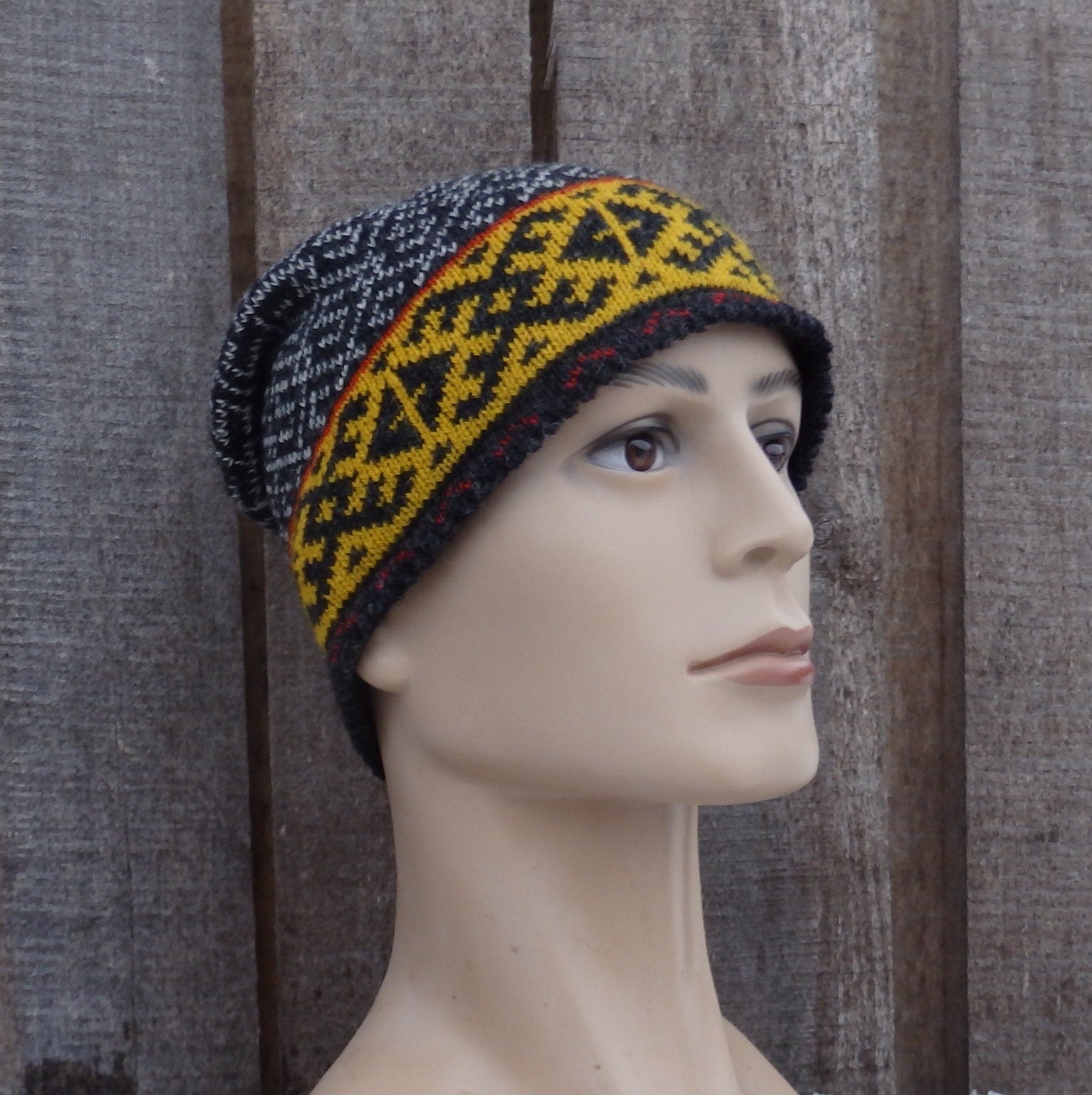 Mannequin head wearing a knitted hat with a geometric pattern against a textured wall.