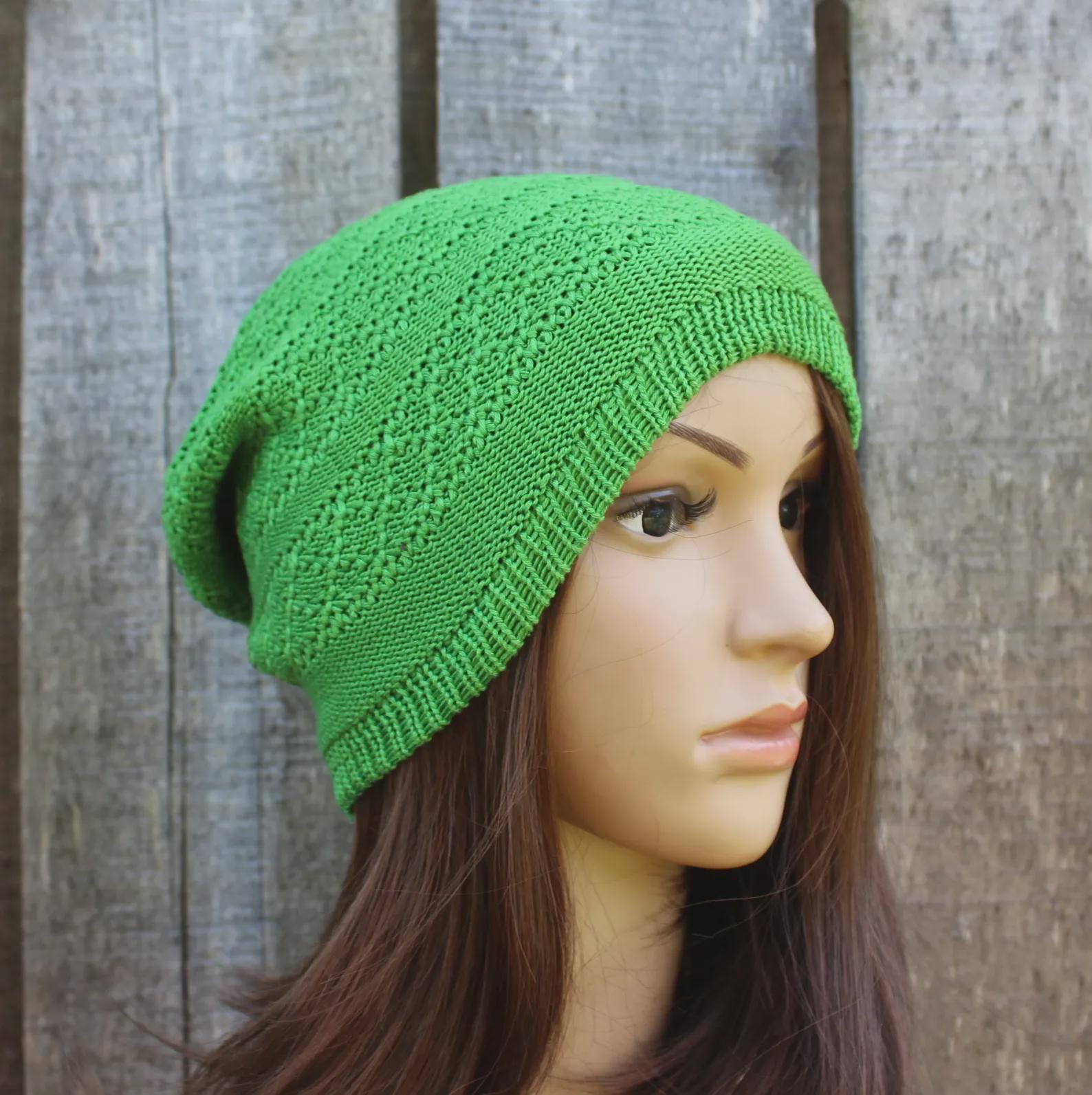 Green knitted beanie on a mannequin head against a wooden background