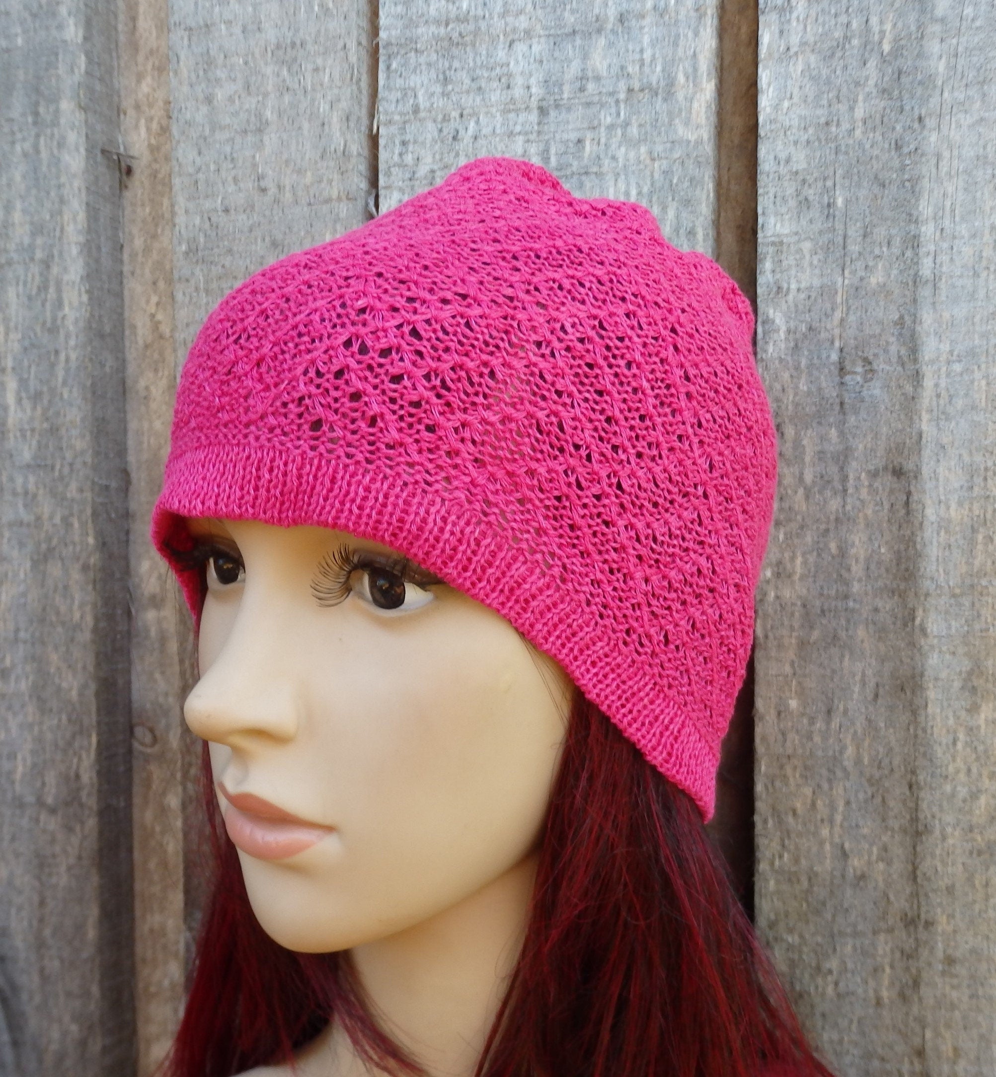 Mannequin head wearing a bright pink knitted hat against a wooden background