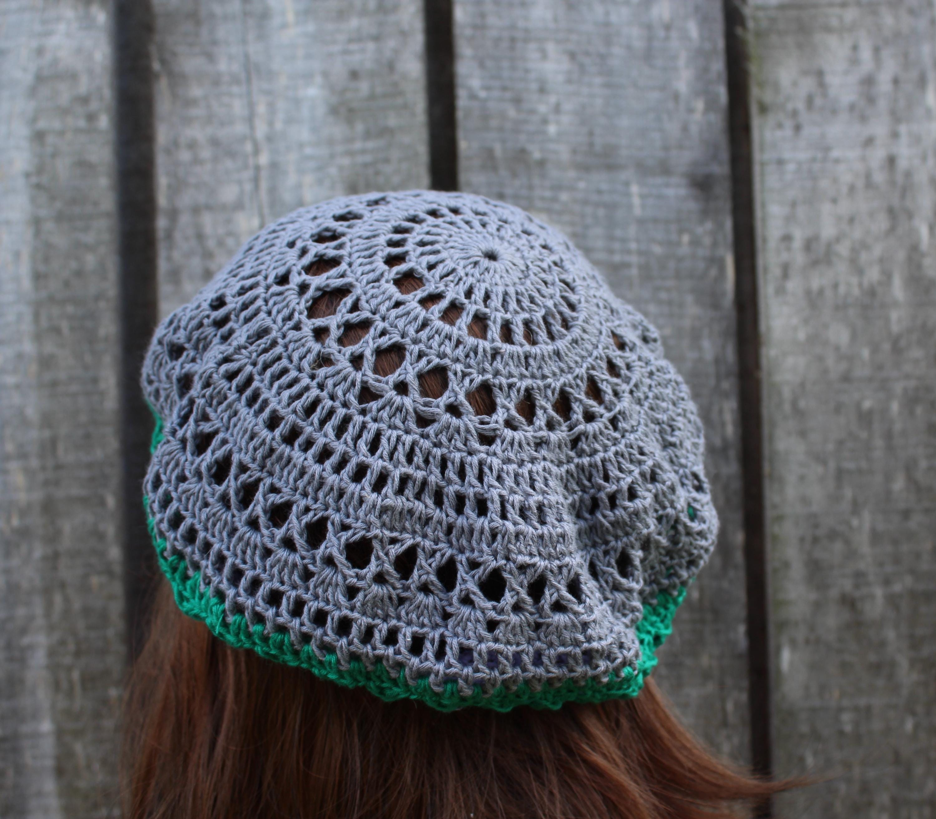 Gray crochet hat with green trim worn by a person against a wooden fence background