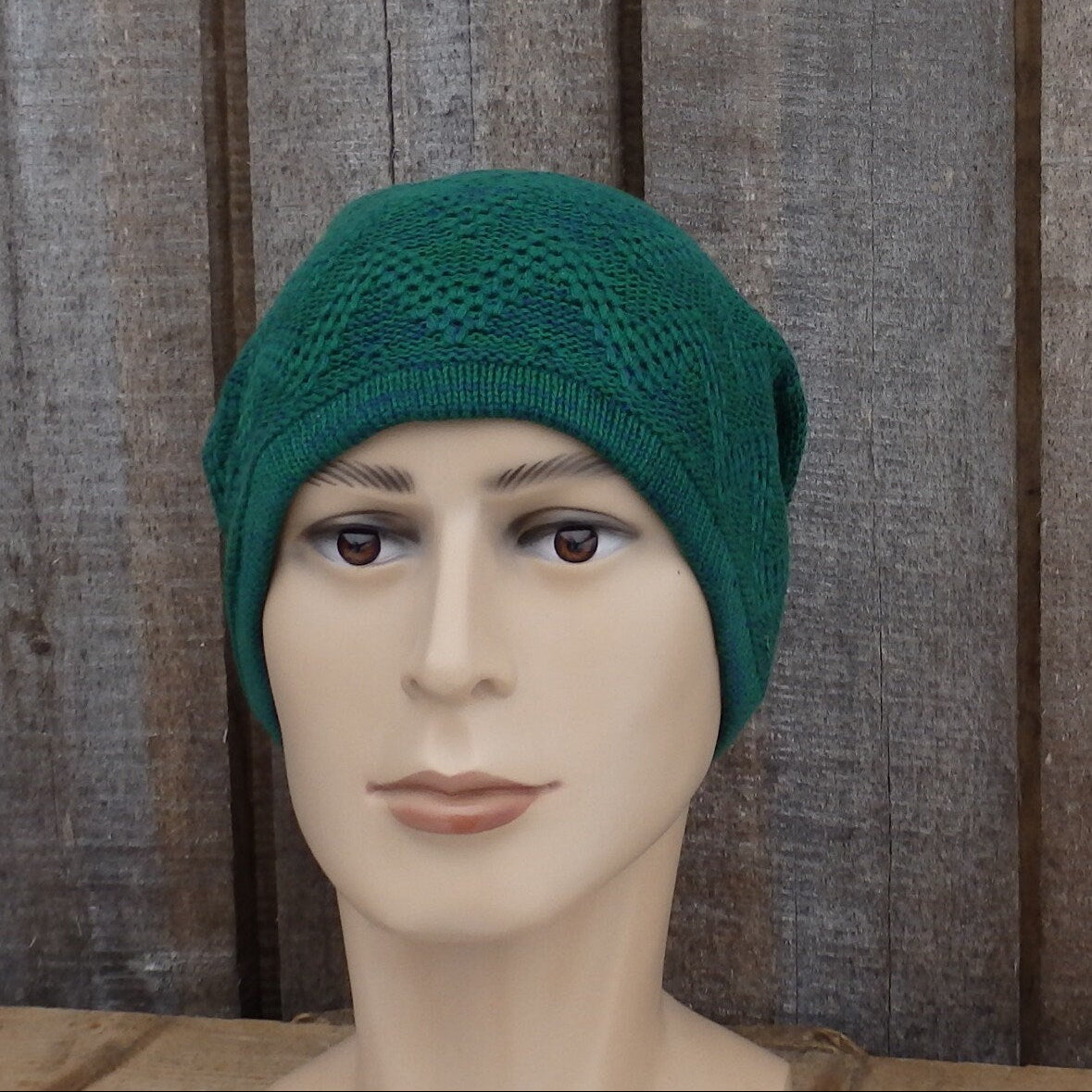 Mannequin head wearing a green knitted hat against a wooden background