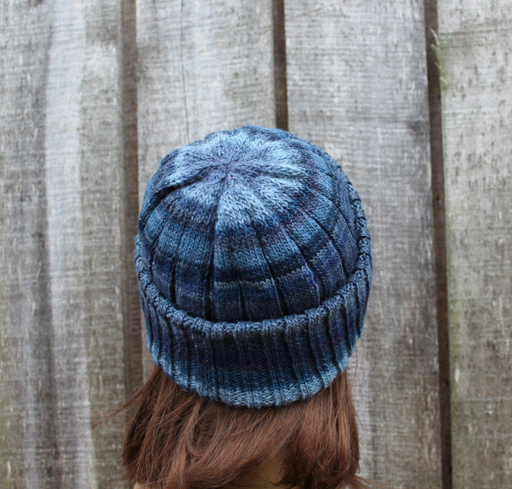 Blue knitted beanie worn by a person against a wooden fence background